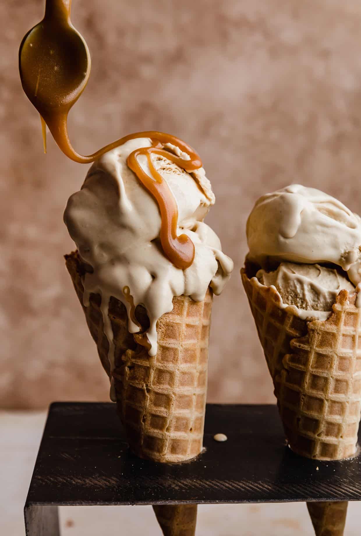 Butterscotch sauce being drizzled overtop Butterscotch Ice Cream that's in a waffle cone.