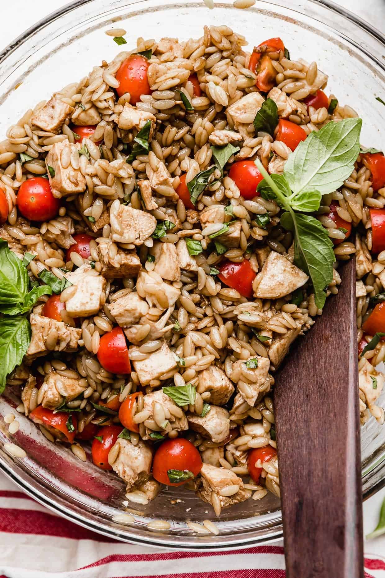chicken orzo caprese salad in a glass bowl on a white background.