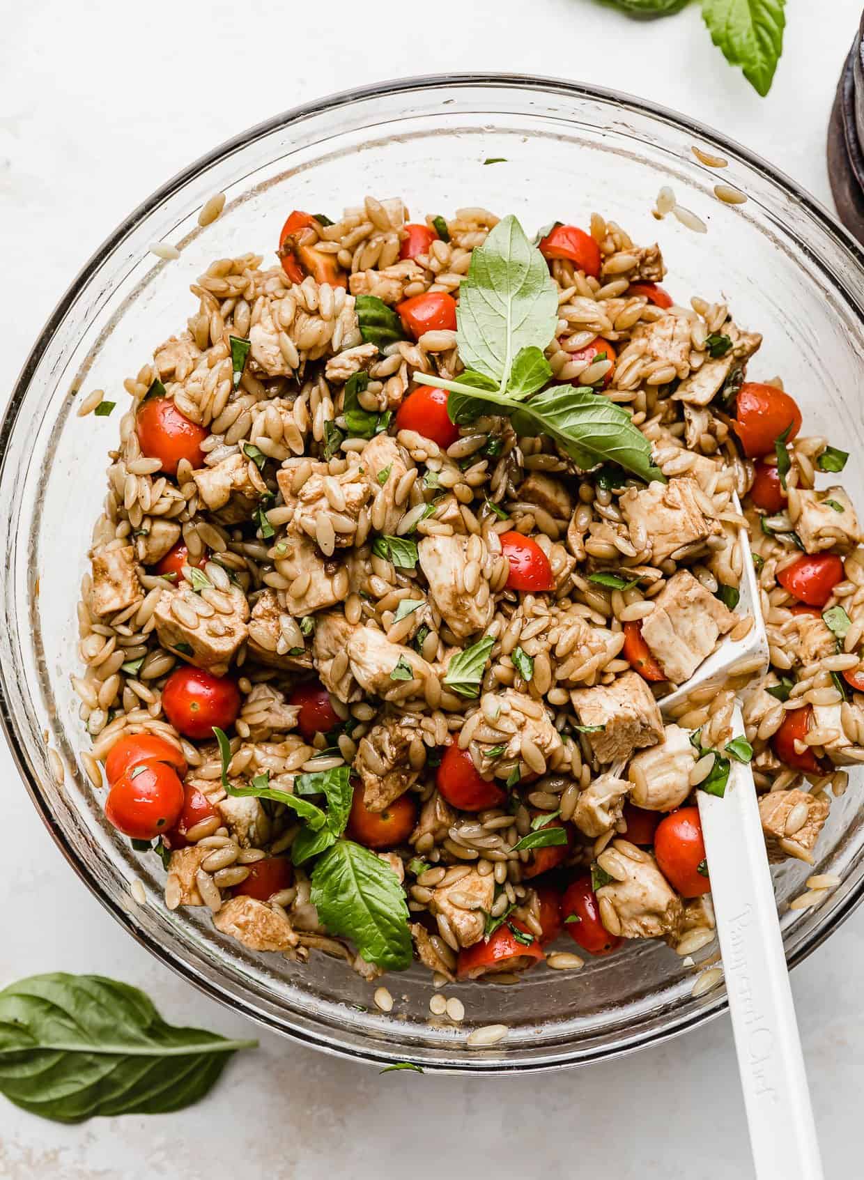 Caprese Orzo Salad in a glass bowl with fresh basil garnish.