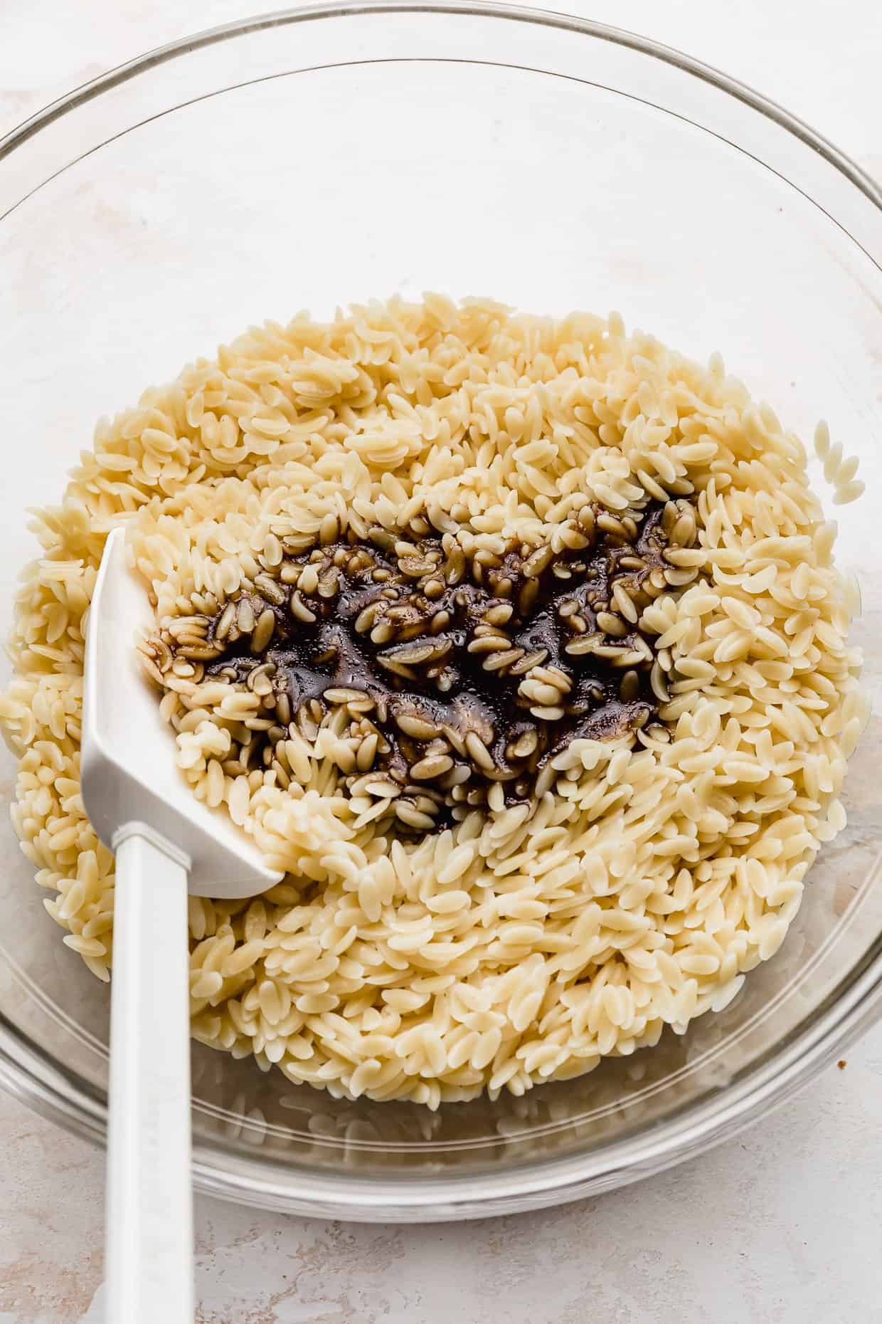 A Caprese Orzo Salad dressing made from balsamic vinegar overtop of the orzo pasta.