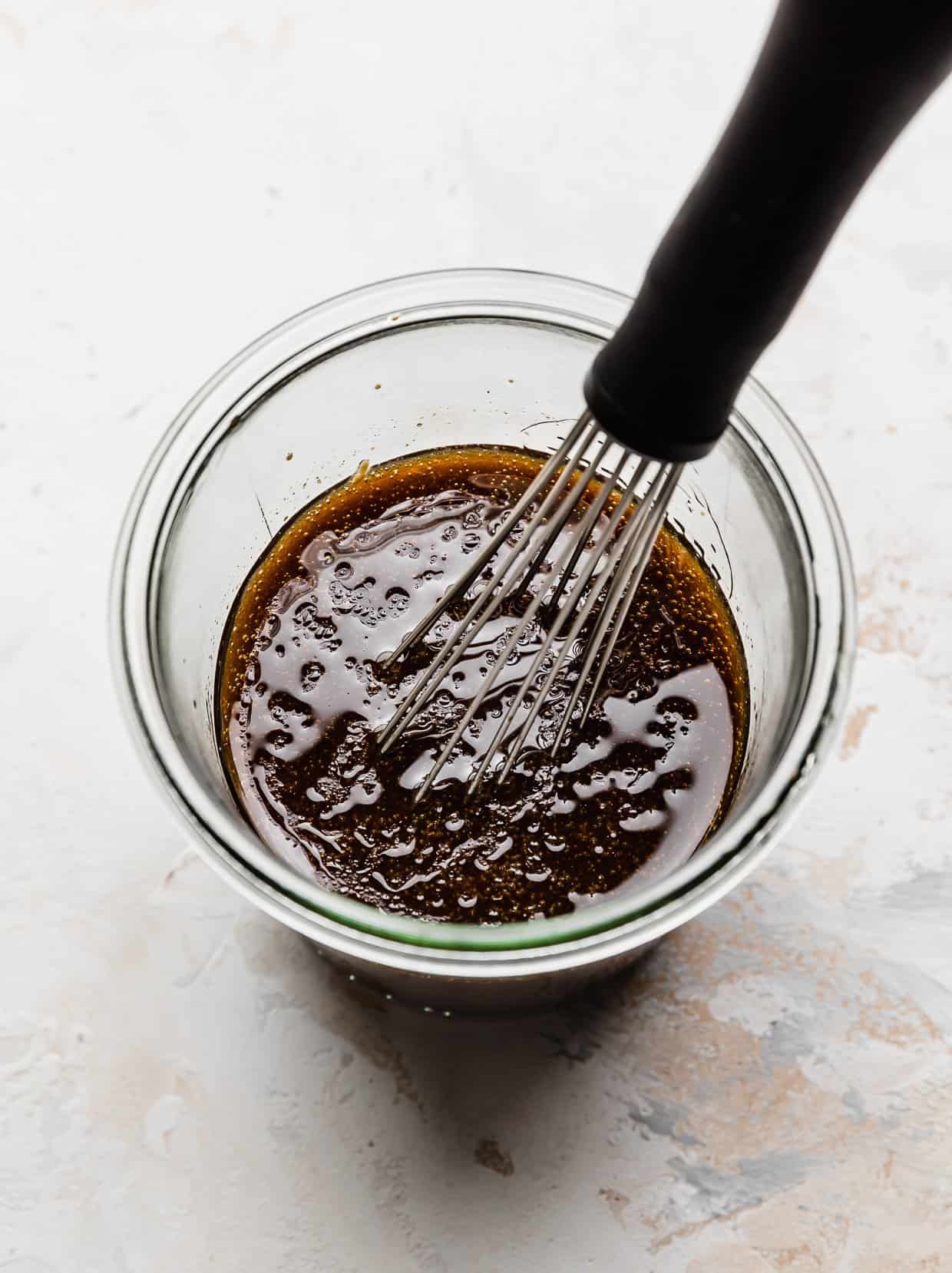 Glass jar on white background that's filled with a Caprese Orzo Salad dressing made with balsamic vinegar and olive oil.