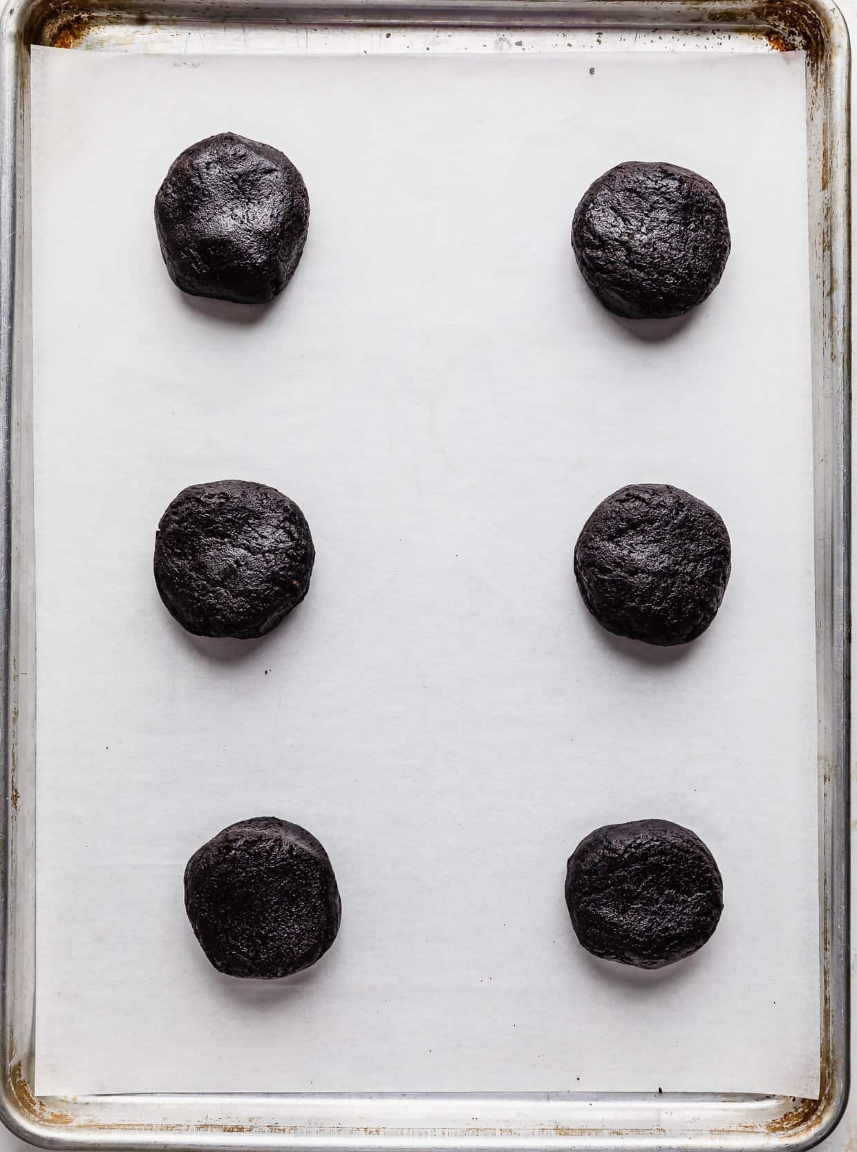 Six Oreo Birthday Cake Cookie dough balls on a white parchment paper.