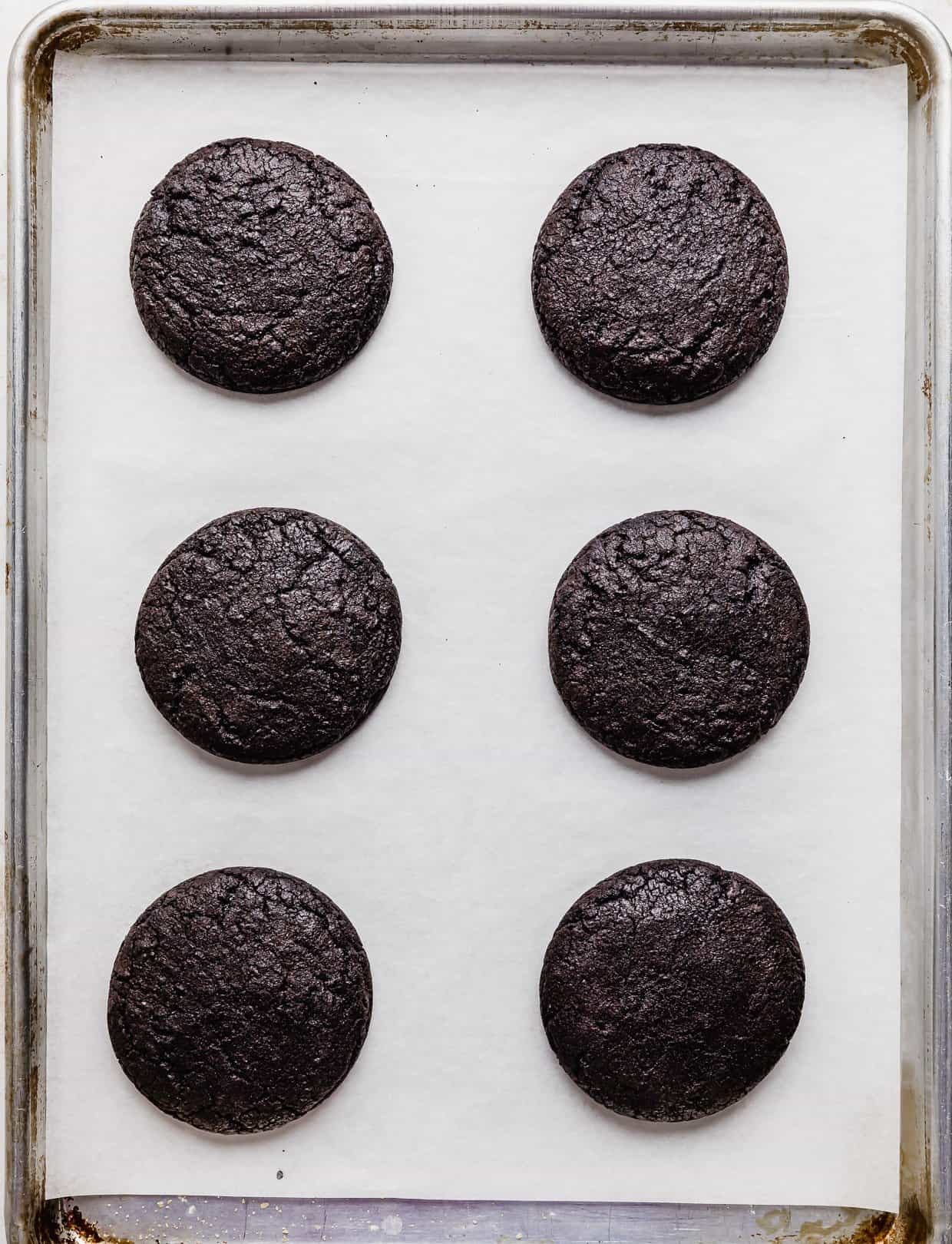 Six baked Crumbl sized Oreo Birthday Cake Cookies on a white parchment lined baking sheet.
