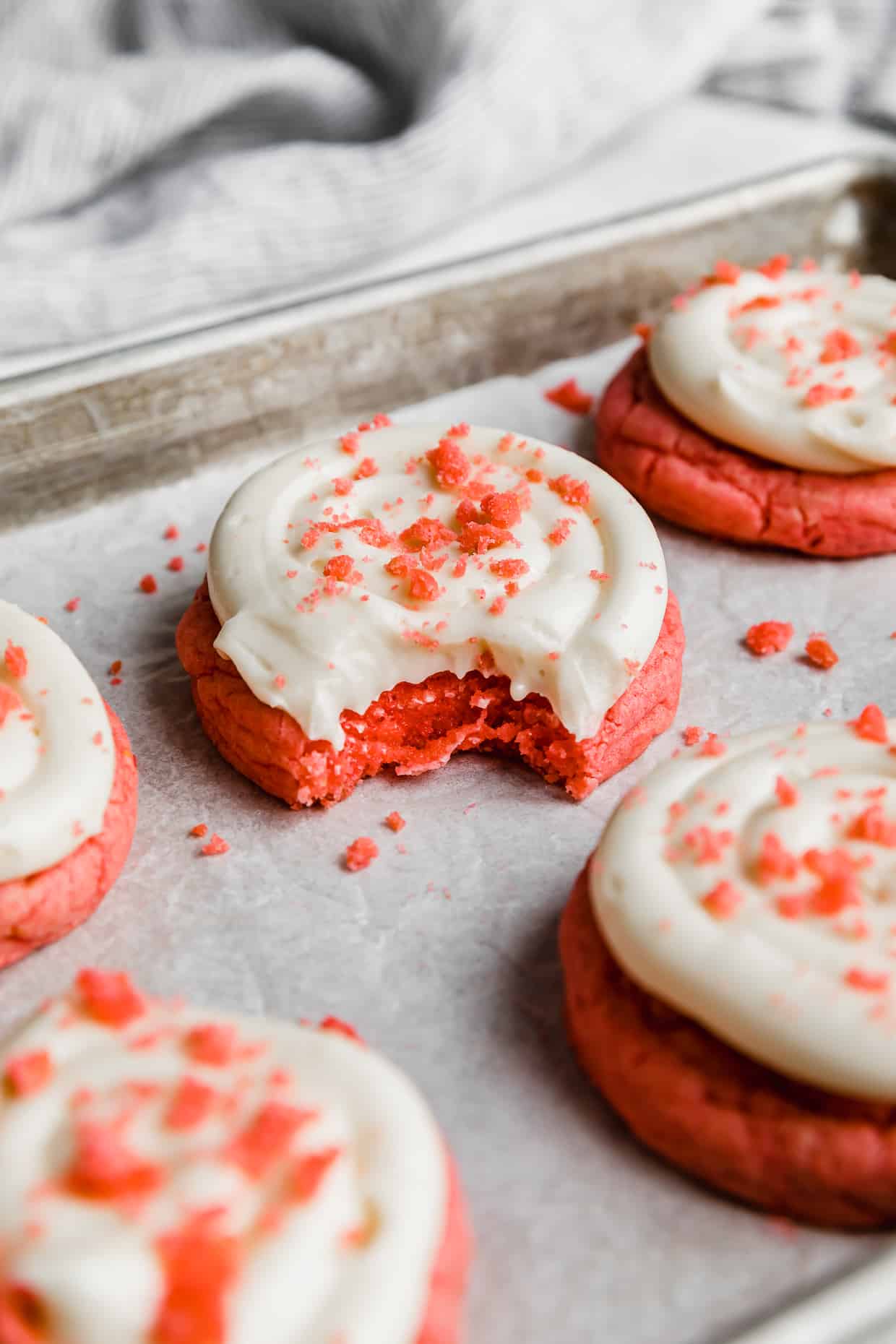A Crumbl Pink Velvet Cookie topped with cream cheese frosting with a bite taken out of the cookie.
