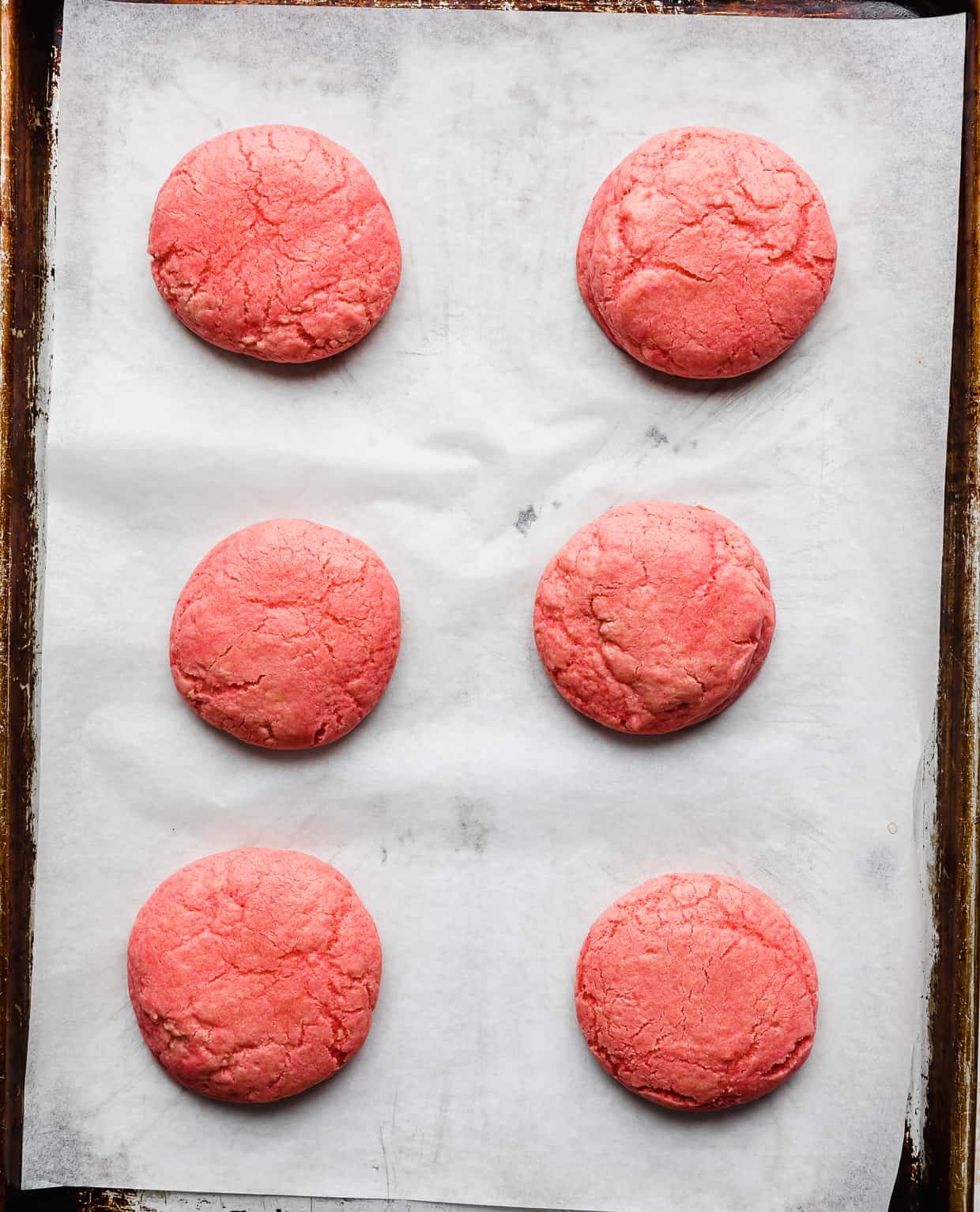 Six pink velvet cookies on a baking sheet.