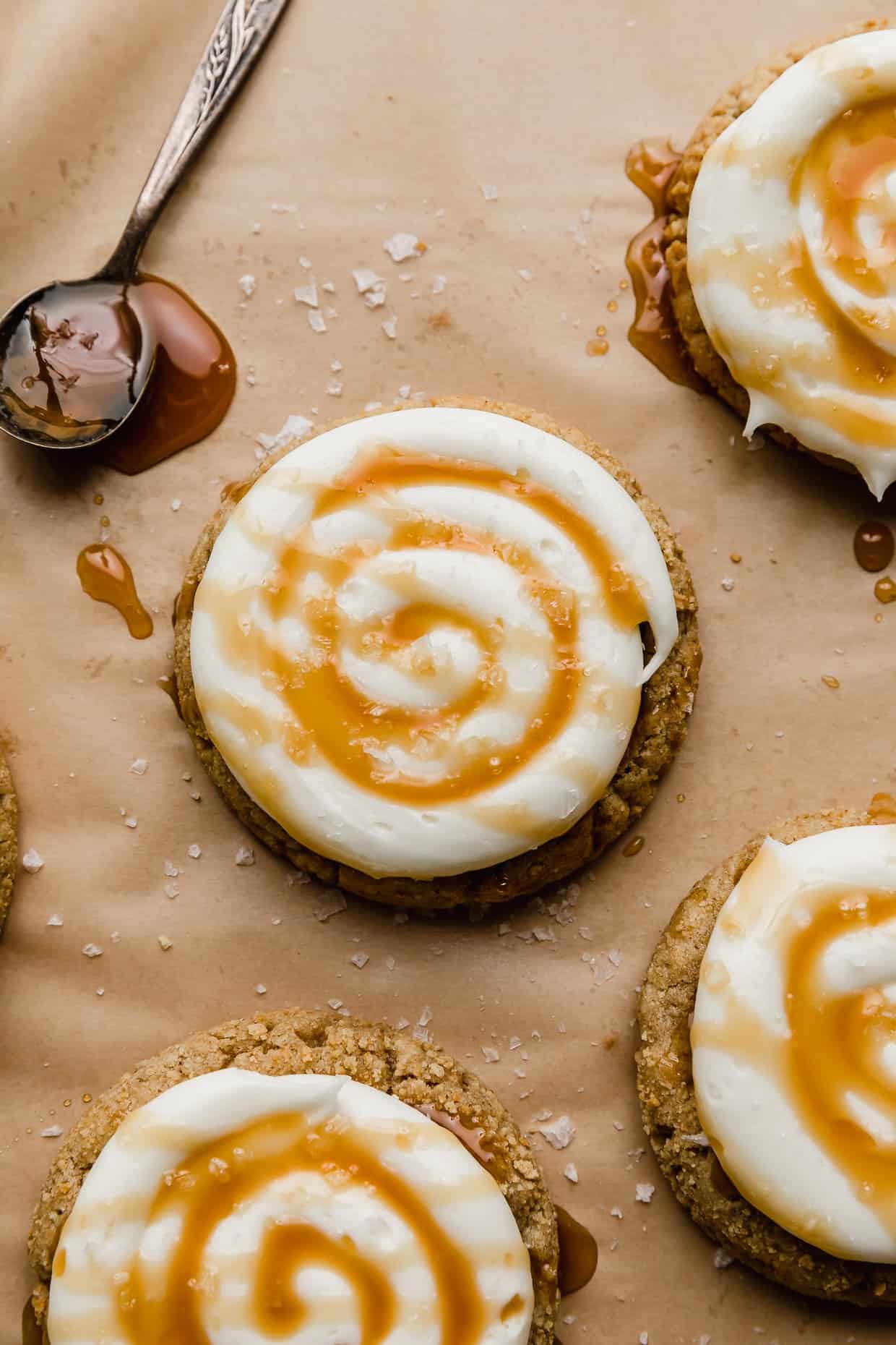 A Crumbl Salted Caramel Cheesecake Cookie topped with cream cheese frosting and caramel on a tan background.