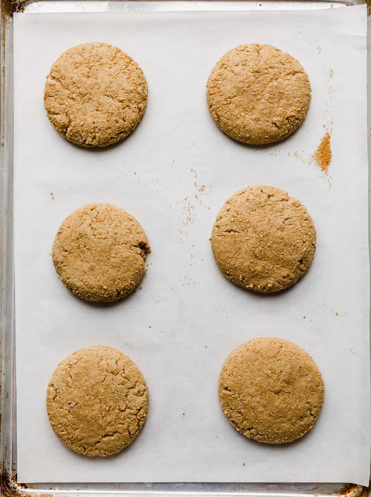 Six baked graham cracker cookies on a white parchment paper lined baking sheet.
