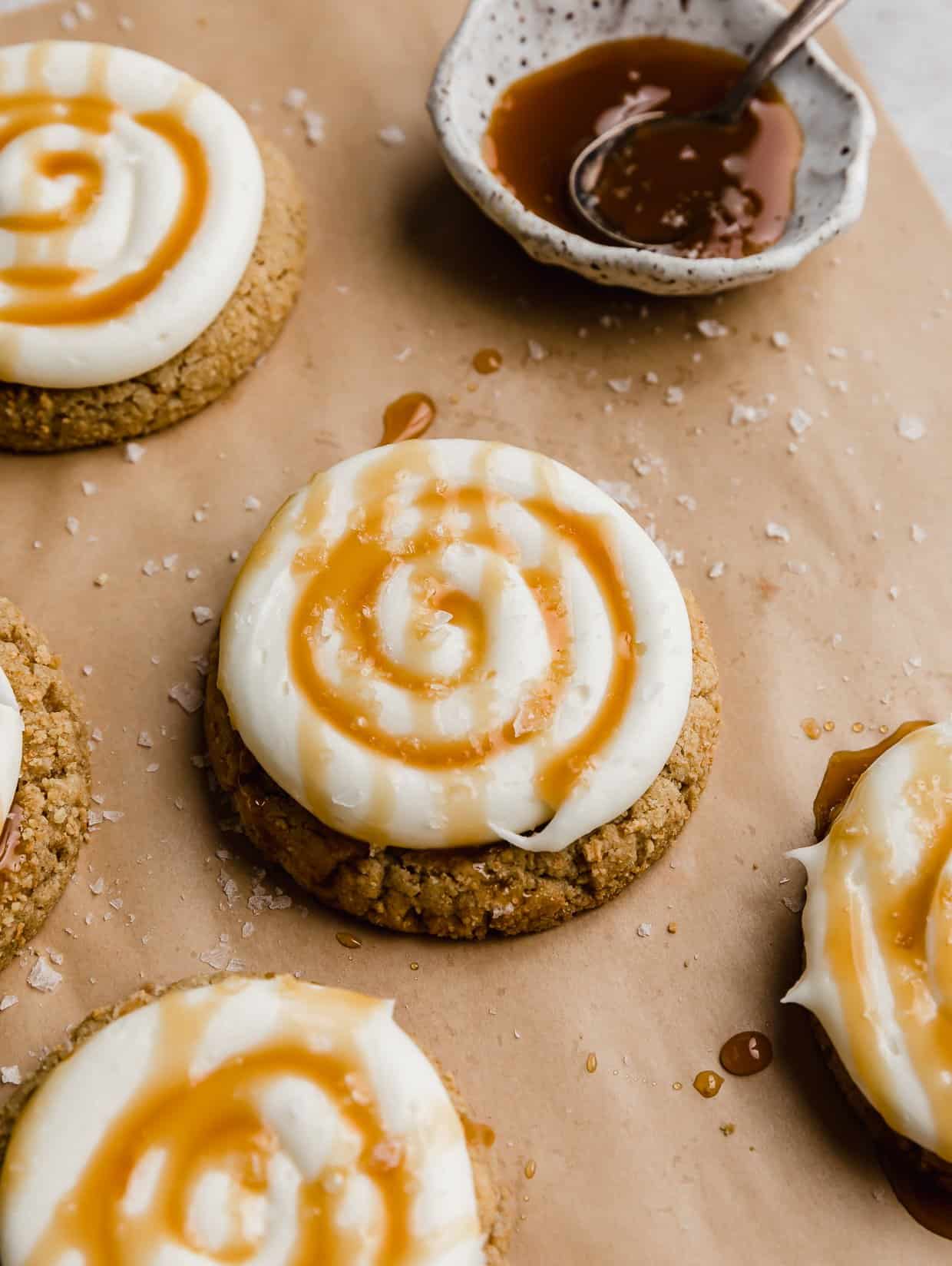 A Crumbl Salted Caramel Cheesecake Cookie topped with white frosting and caramel and salt.