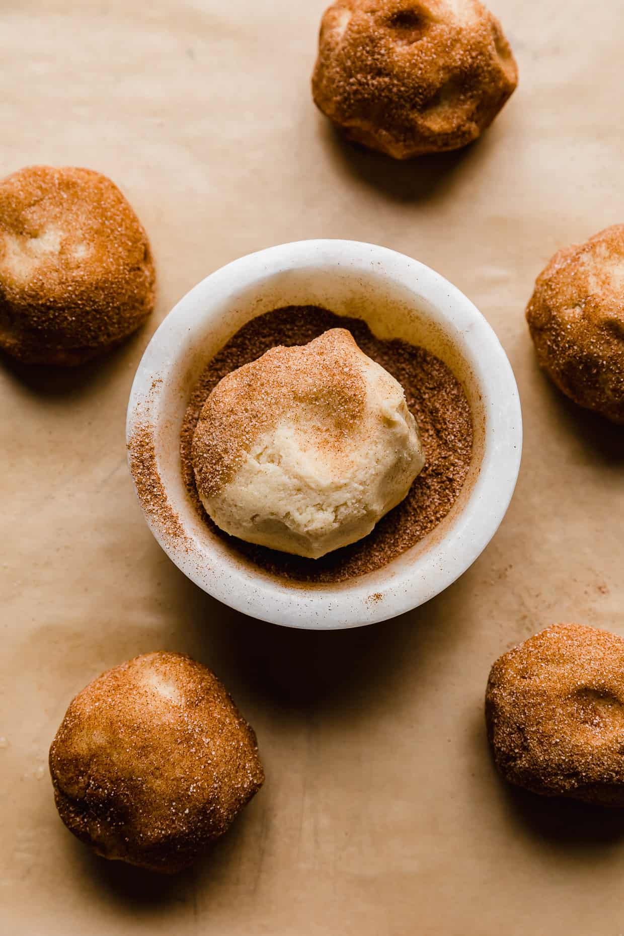 A cookie dough ball in a bowl filled with cinnamon sugar.