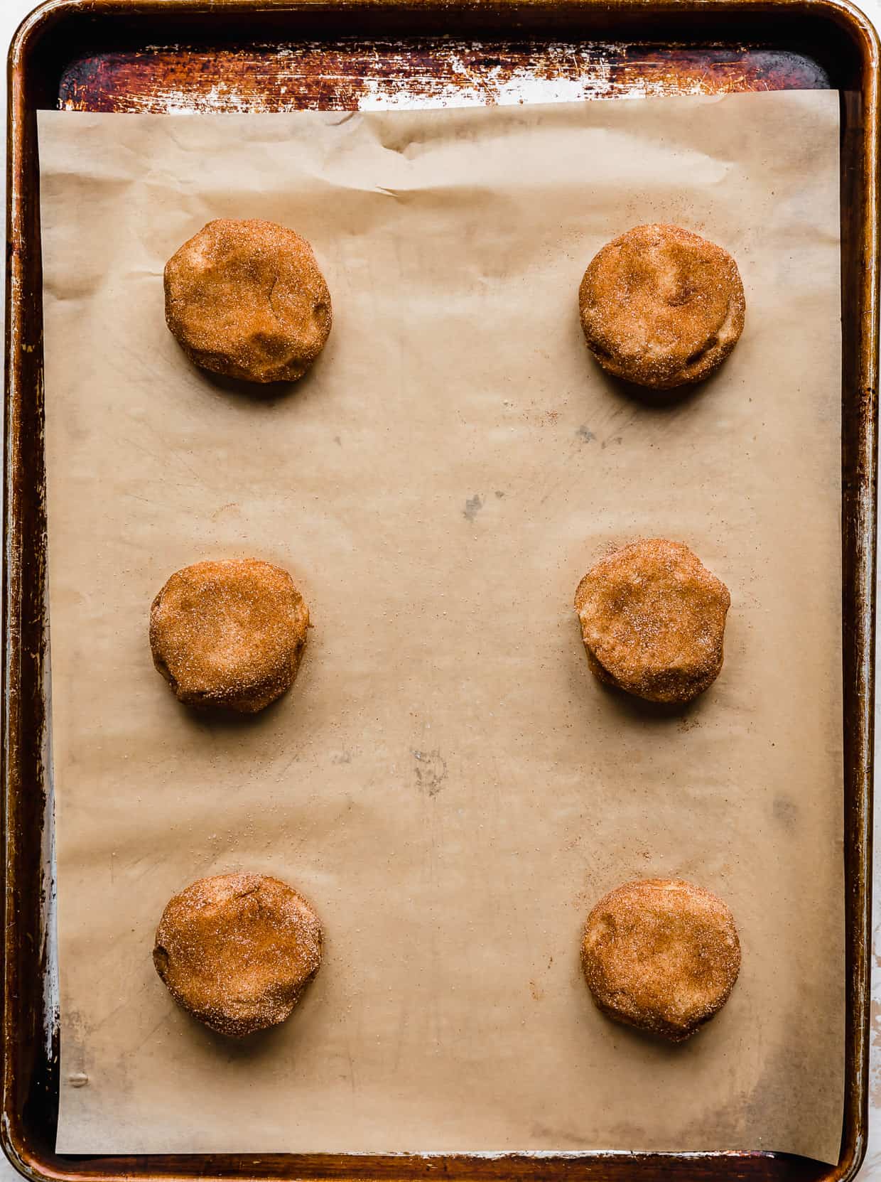 Six Crumbl Snickerdoodle cookie dough balls on a tan parchment paper.