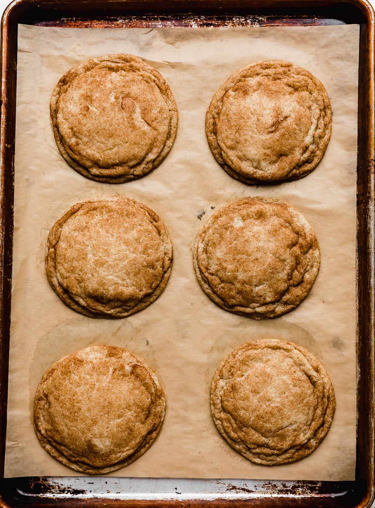Six baked large snickerdoodle cookies on a baking sheet.