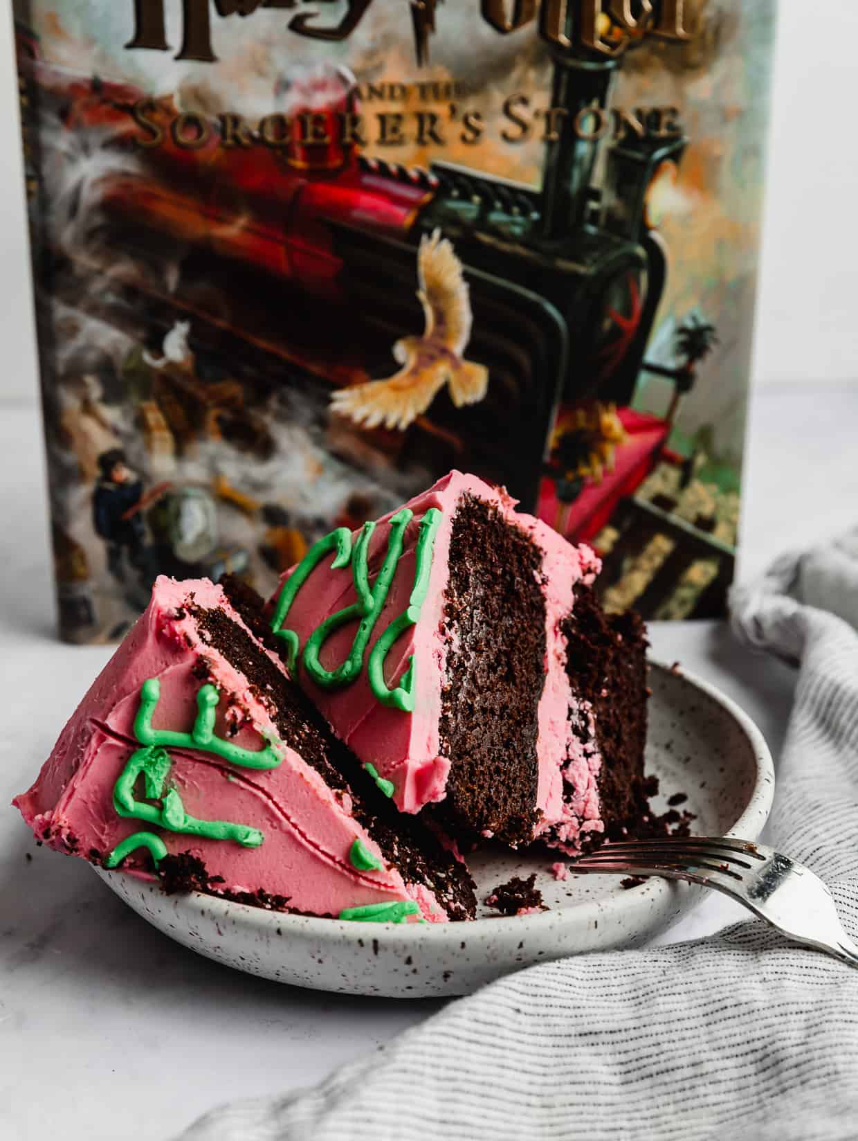 Harry Potters Birthday Cake decorated in pink icing and green lettering, cut into wedges on a white plate with a Harry Potter book in the background.