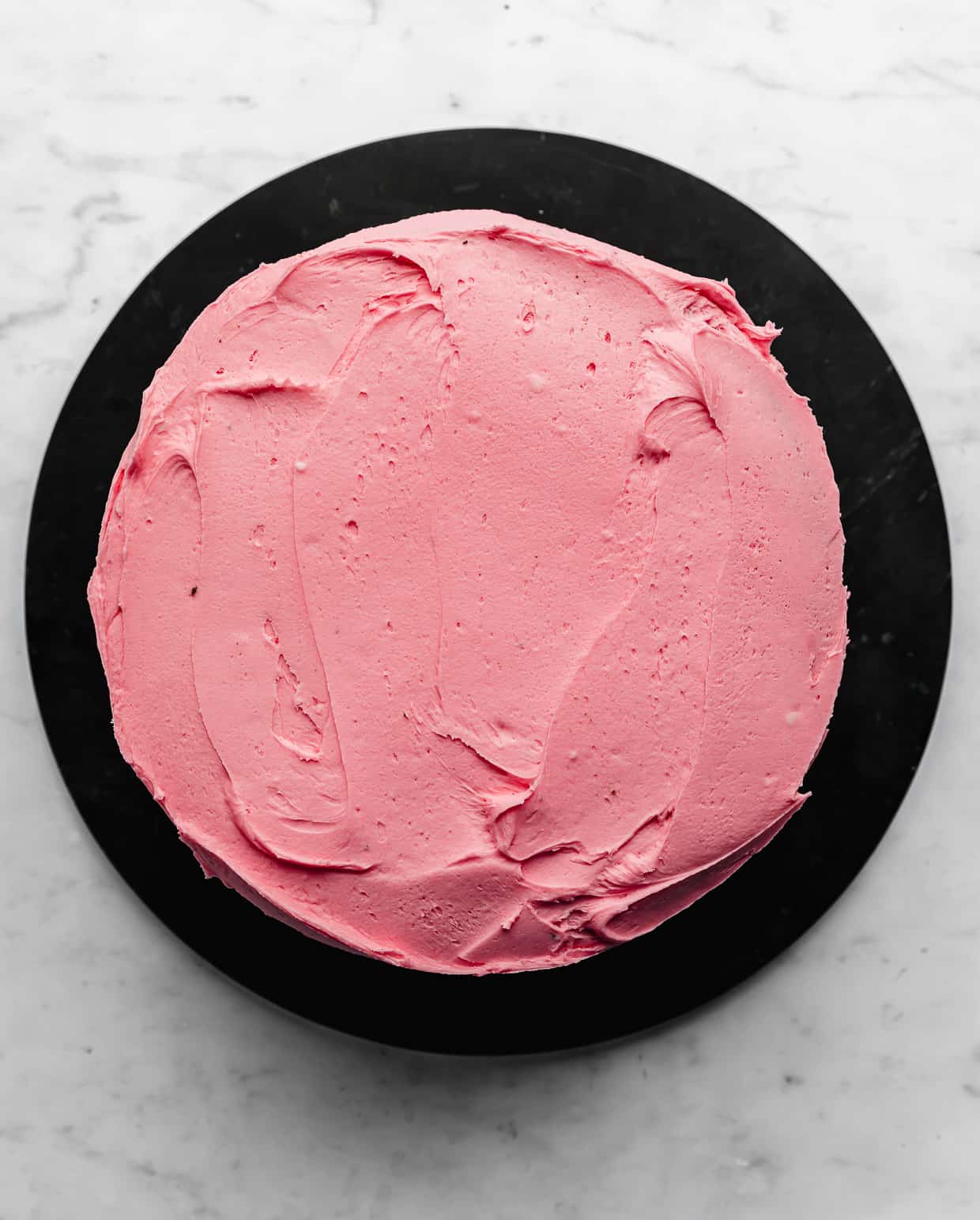 Overhead photo of a round cake frosted in pink frosting.
