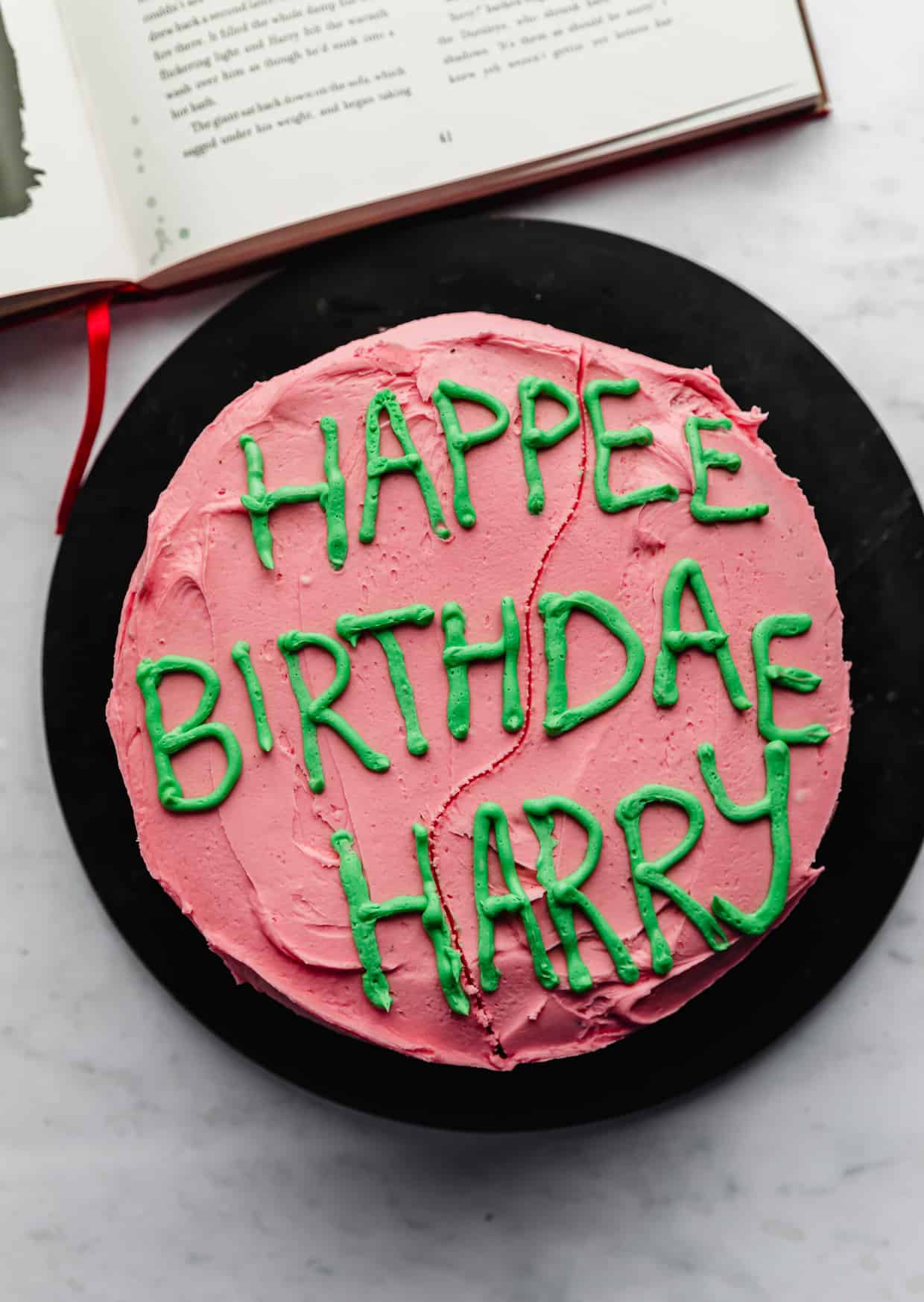 A pink cake with green frosting writing "Happy birthdae Harry".