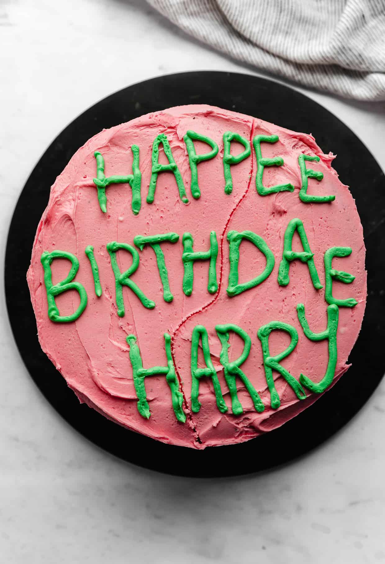 Happee Birthdae Harry written in green frosting on a pink cake.