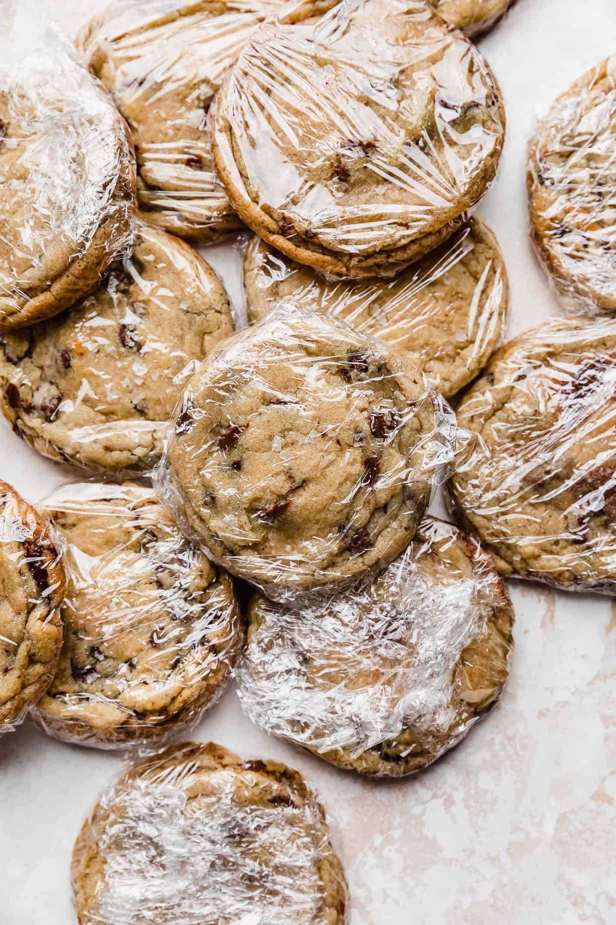 Baked chocolate chip cookies individually wrapped in plastic wrap, showcasing the proper way on how to freeze baked cookies.