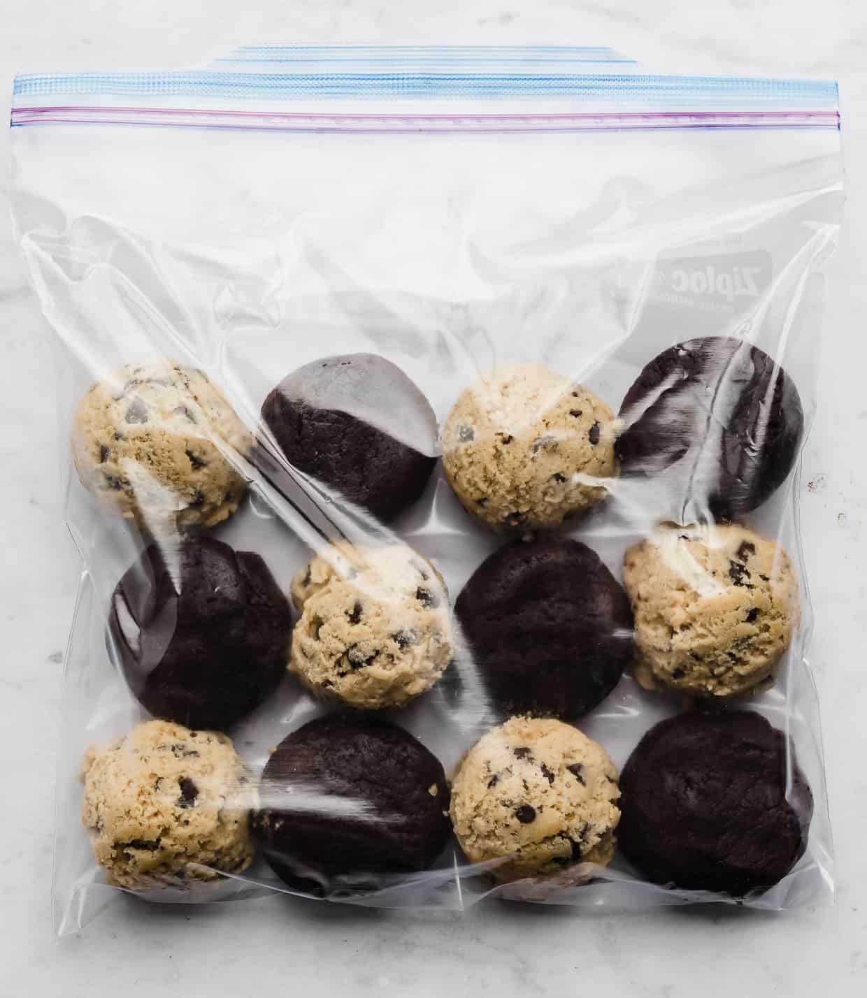 A ziplock bag with frozen chocolate chip cookie dough balls and frozen brownie batter balls in it.
