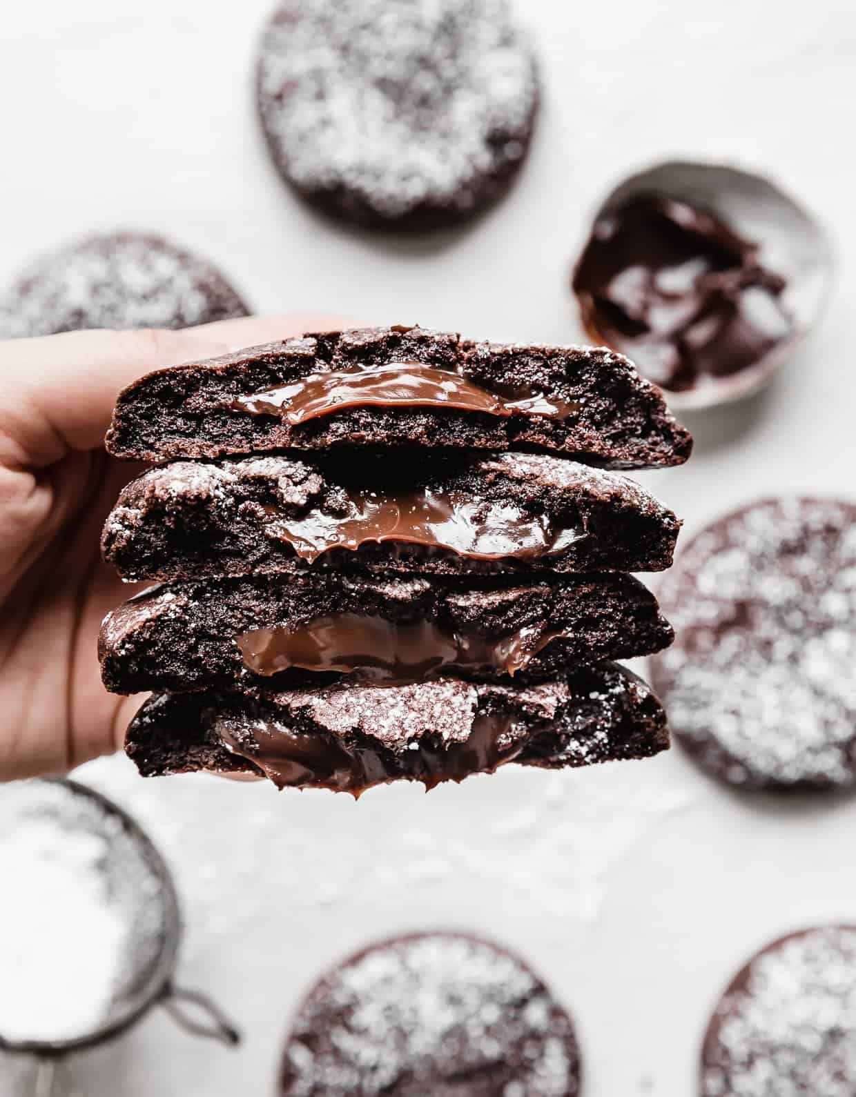 A hand holding four chocolate molten lava cookie halves, with hot fudge oozing from the centers of each half.