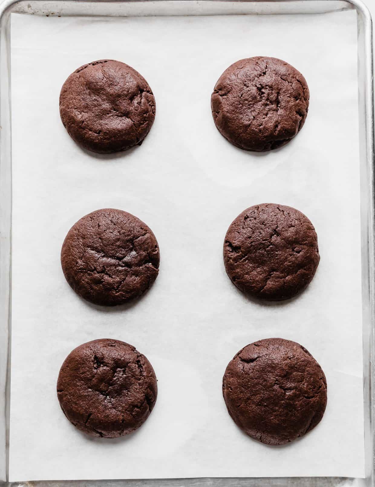 Six baked chocolate molten lava cookies on a white parchment paper.