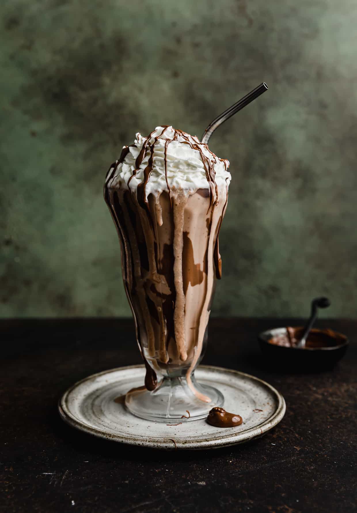 A glass cup with Nutella Milkshake in it, against a dark green textured background.