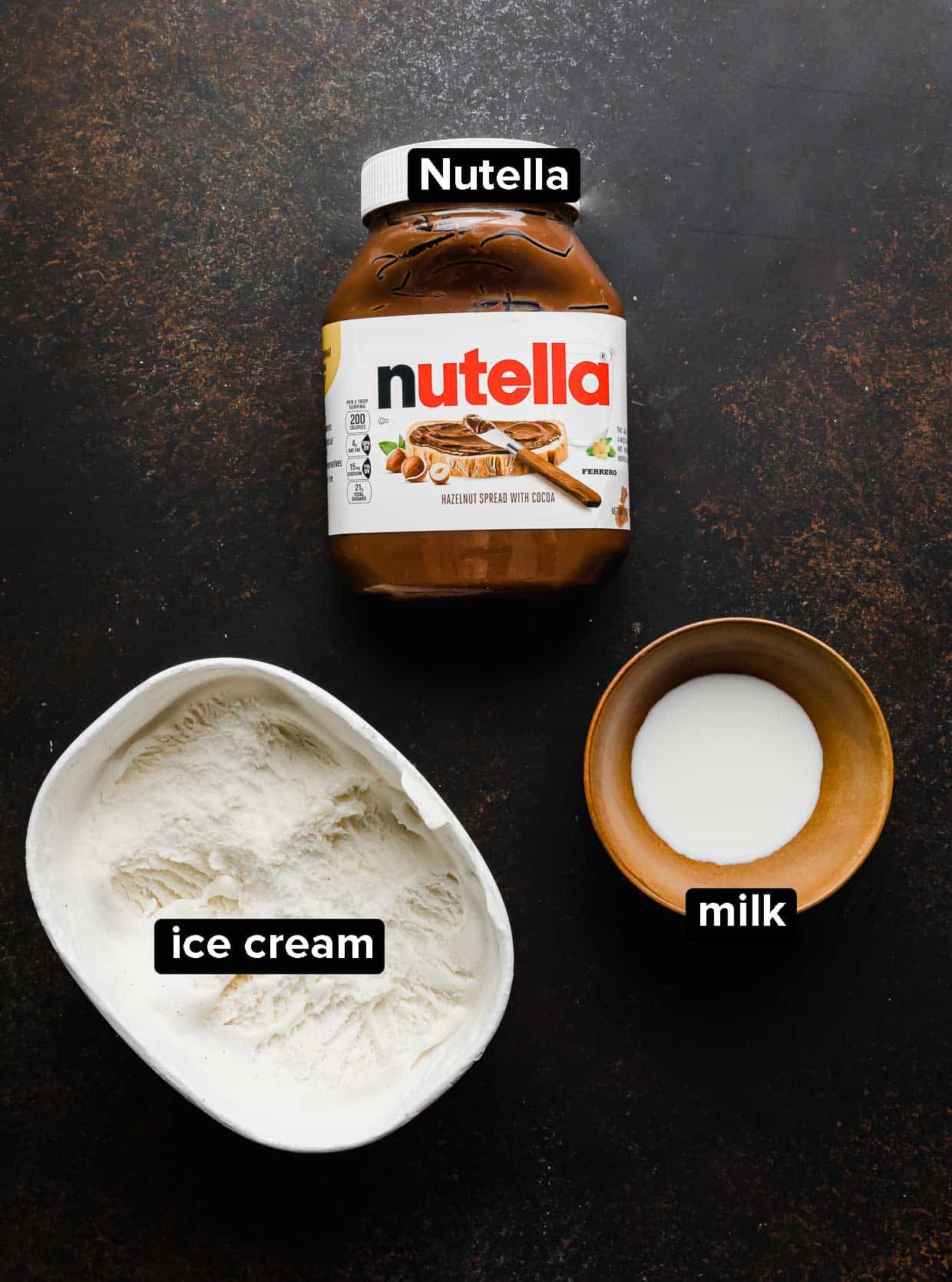 Nutella Milkshake ingredients: Nutella, vanilla ice cream, and milk, on a dark brown background.