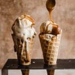 Two waffle cones filled with Butterscotch Ice Cream and topped with butterscotch sauce, against a light brown background.
