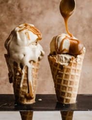 Two waffle cones filled with Butterscotch Ice Cream and topped with butterscotch sauce, against a light brown background.