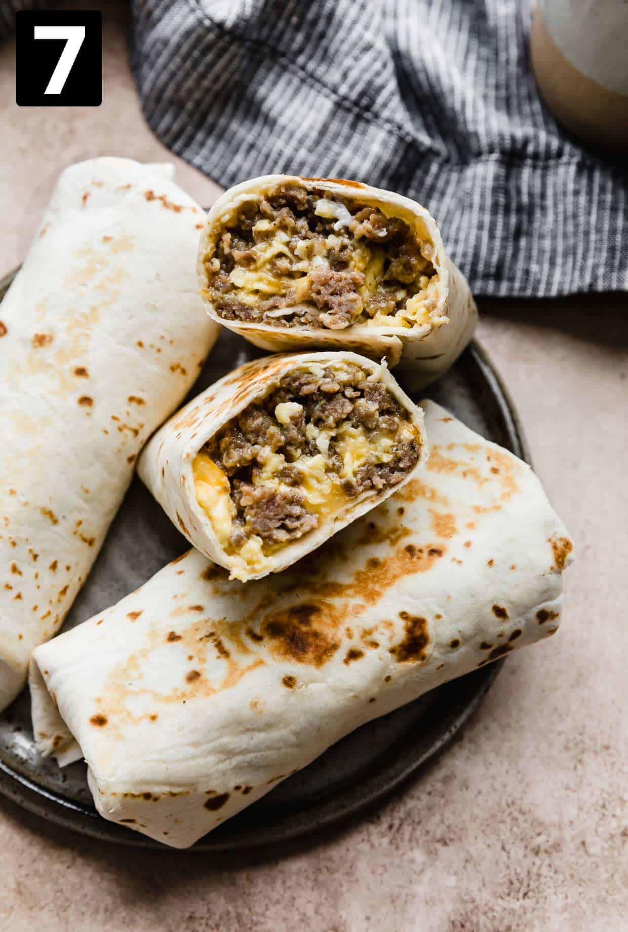A Jimmy Dean Breakfast Burrito cut in half on a gray plate on a tan background.