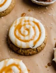 A Salted Caramel Cheesecake Cookie on a tan parchment paper, cookie is topped with caramel and white frosting.