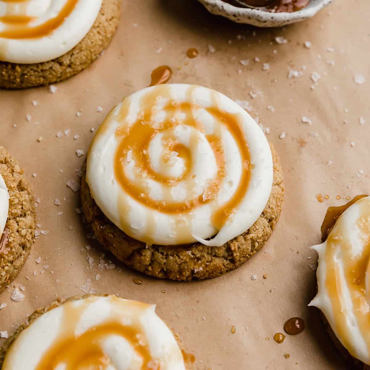 A Salted Caramel Cheesecake Cookie on a tan parchment paper, cookie is topped with caramel and white frosting.