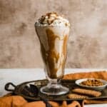 A lotus Biscoff shake in a glass cup topped with whipped cream and crushed Biscoff cookies.