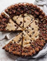 A Chocolate Chip Cookie Cake in a pie plate with chocolate frosting along the edges and sprinkles overtop.