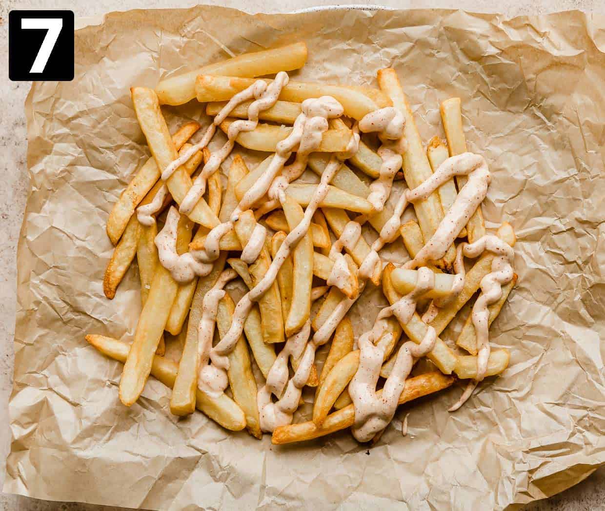 Fries with crema drizzled overtop on a tan parchment paper