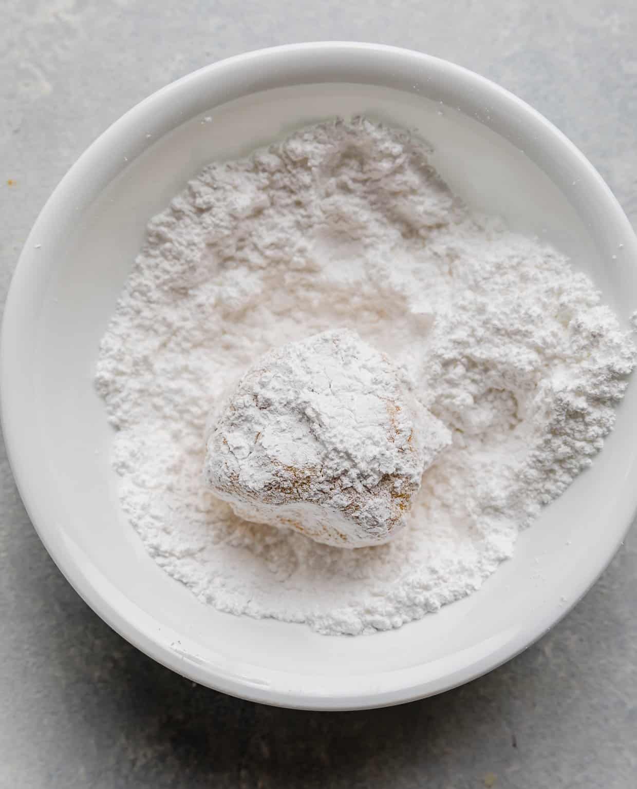 A lemon crinkle cookie dough ball rolled in powdered sugar.