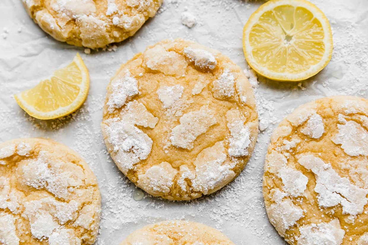 Lemon Crinkle Cookies on a white parchment paper with 2 lemon slices by the cookies.