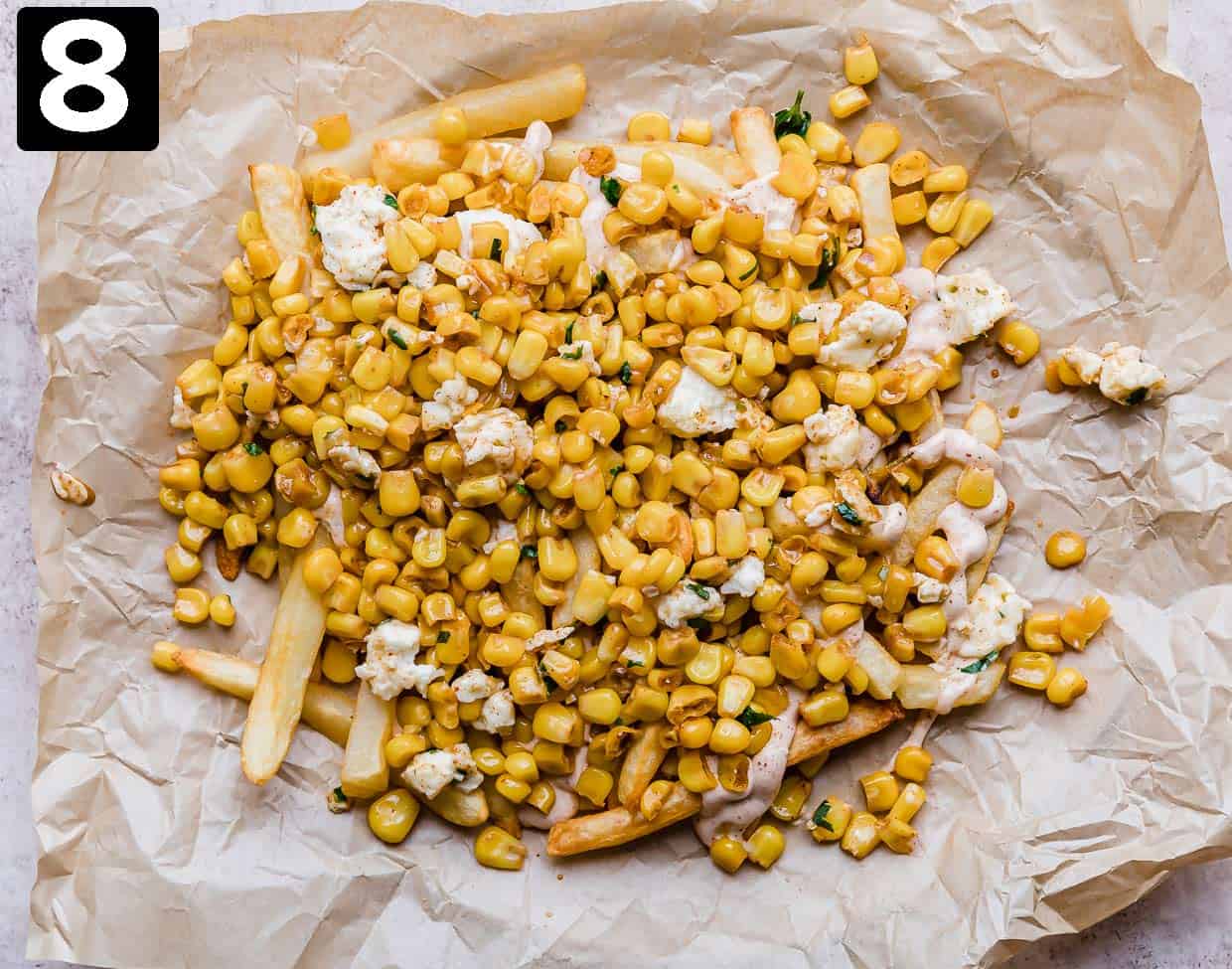 Fries topped with a Mexican Street Corn mixture on a parchment paper.