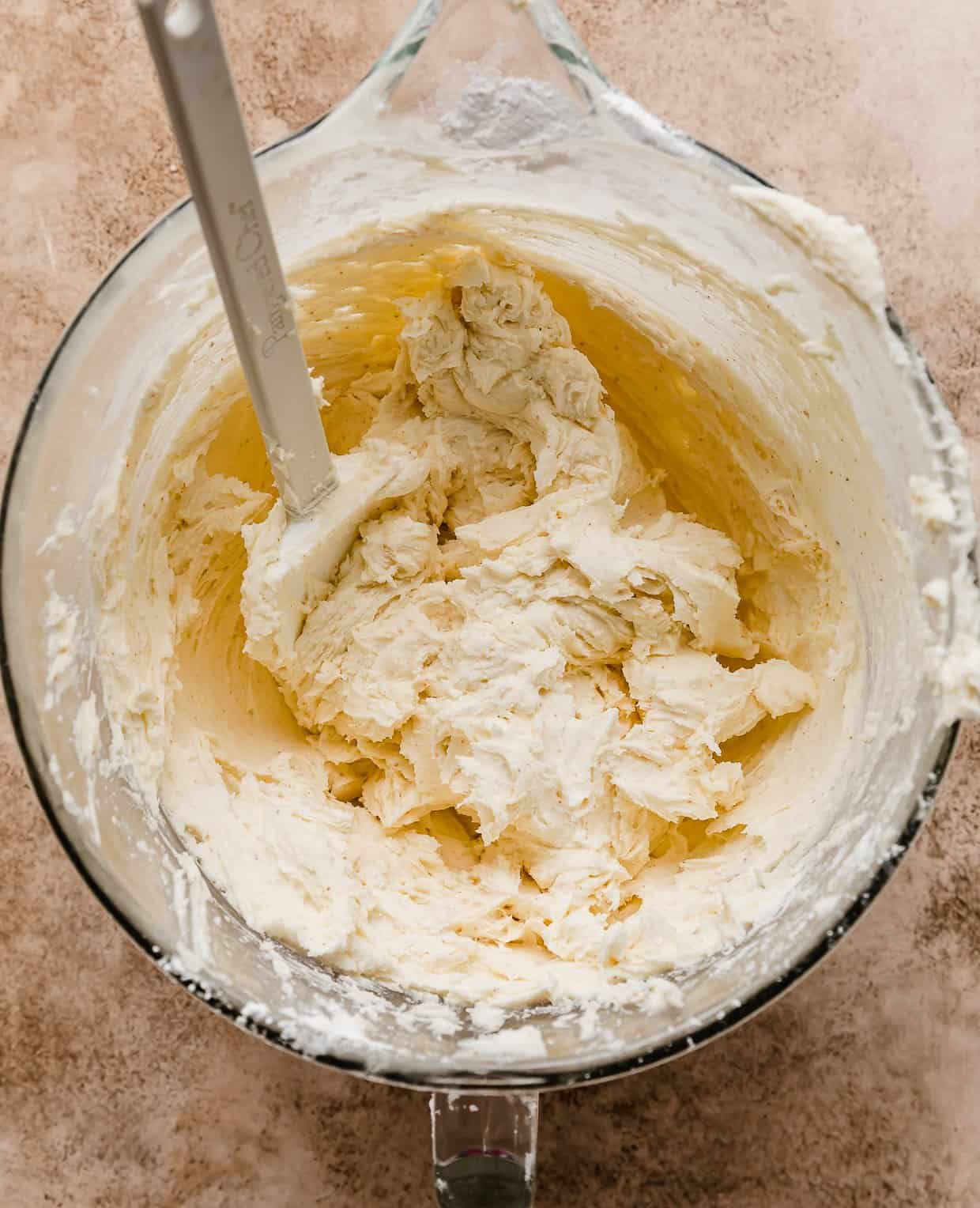 Brown butter frosting in a glass bowl with a white spatula in the bowl.