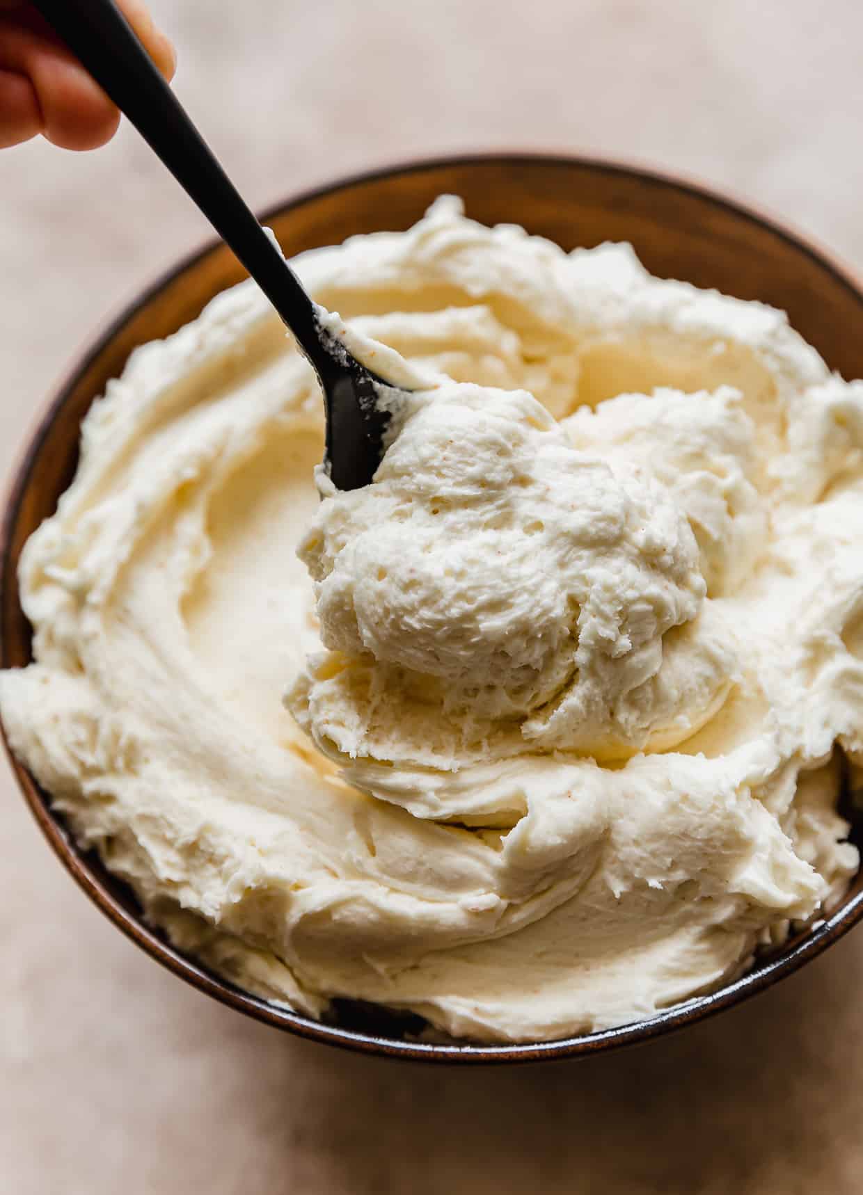 A spoon scooping brown butter frosting from a bowl filled with buttercream.