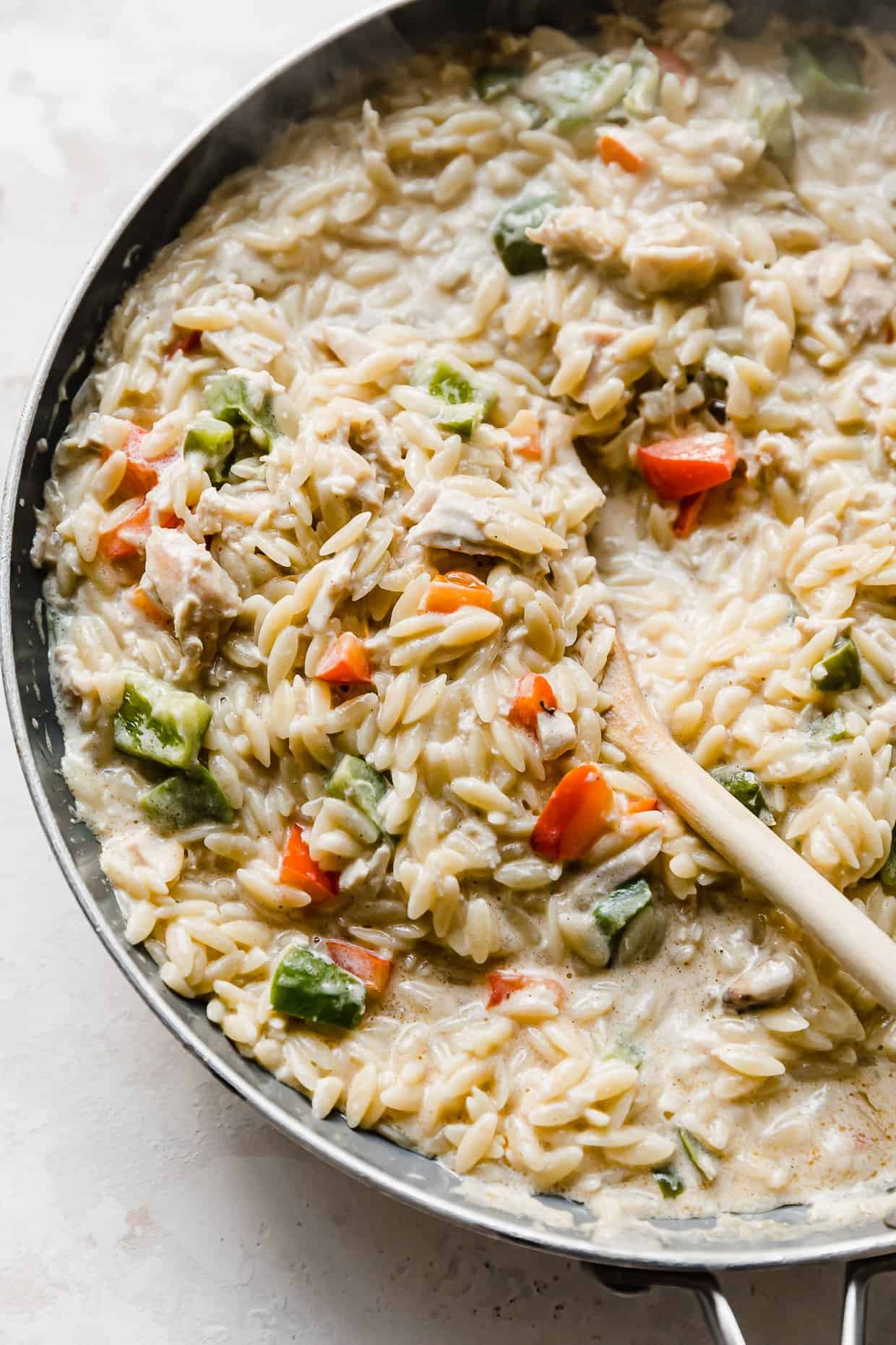 Cajun Chicken Orzo in a skillet with a wooden spoon scooping into the noodles.