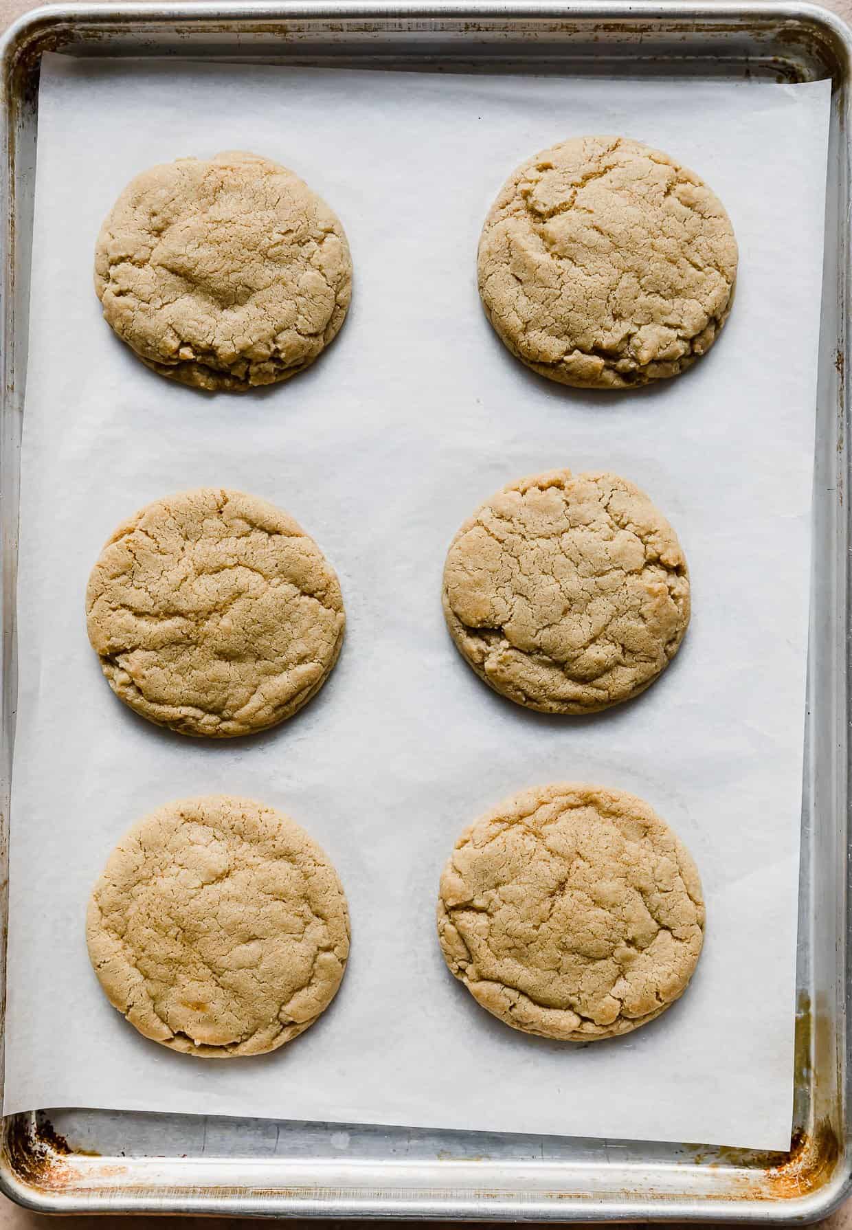 Six baked Cookie Butter Cookies on a white parchment lined baking sheet.