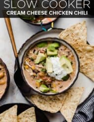 A bowl of Crock Pot Cream Cheese Chicken Chili topped with sour cream and avocado, with the words "slow cooker cream cheese chicken chili" written in white text over the photo.