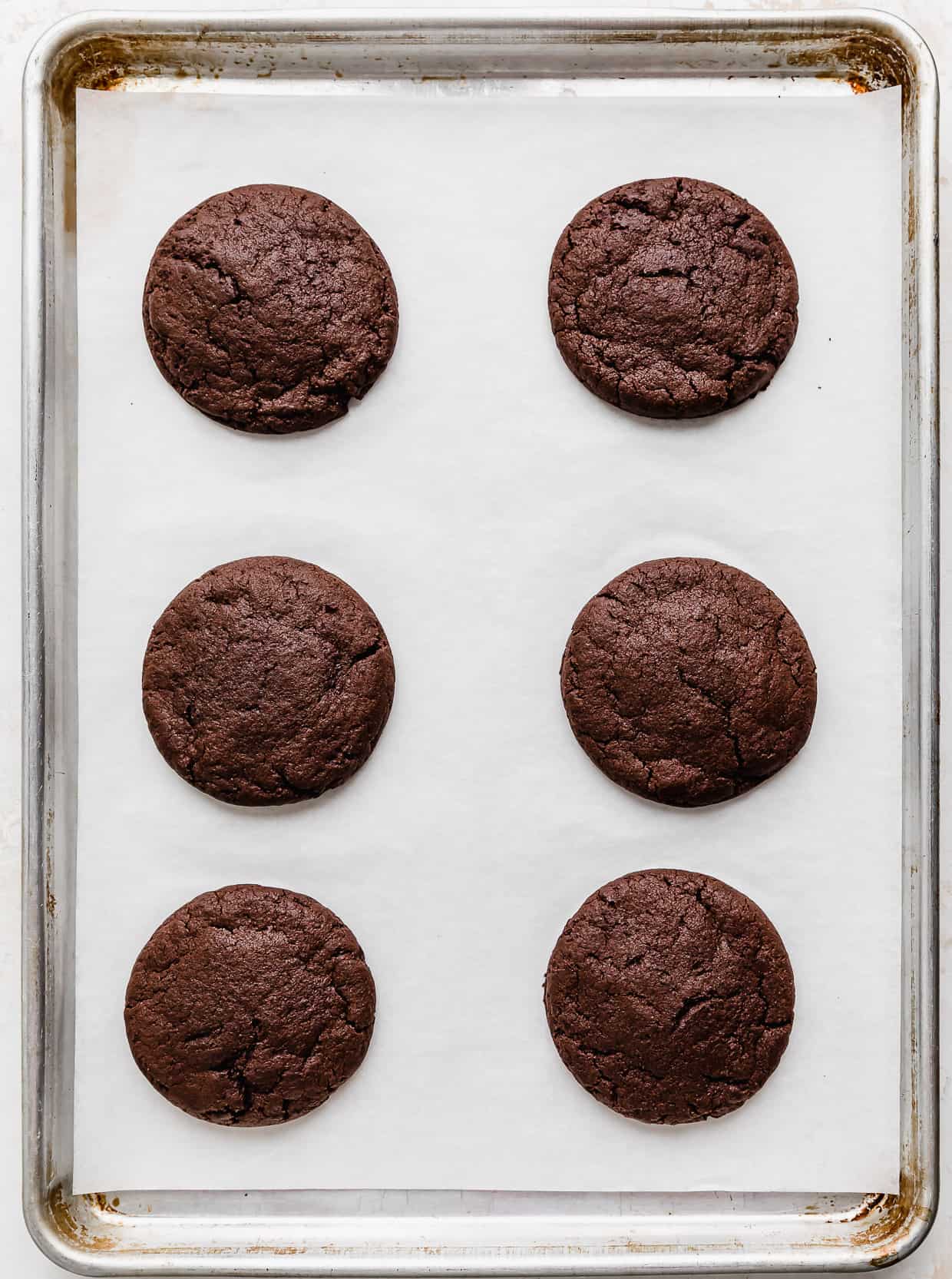 Six baked chocolate cookies on a white parchment paper lined baking sheet.