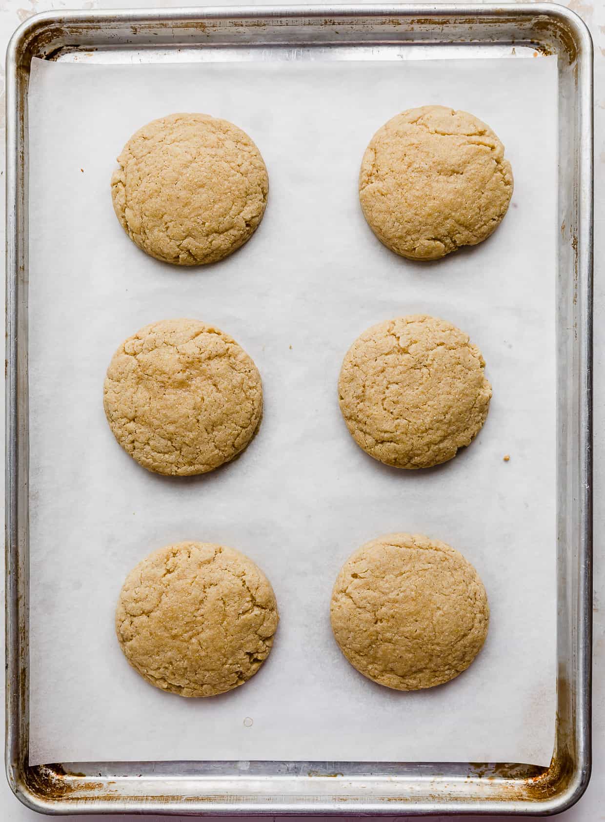 Six baked crumbl cornbread cookies on a baking sheet.
