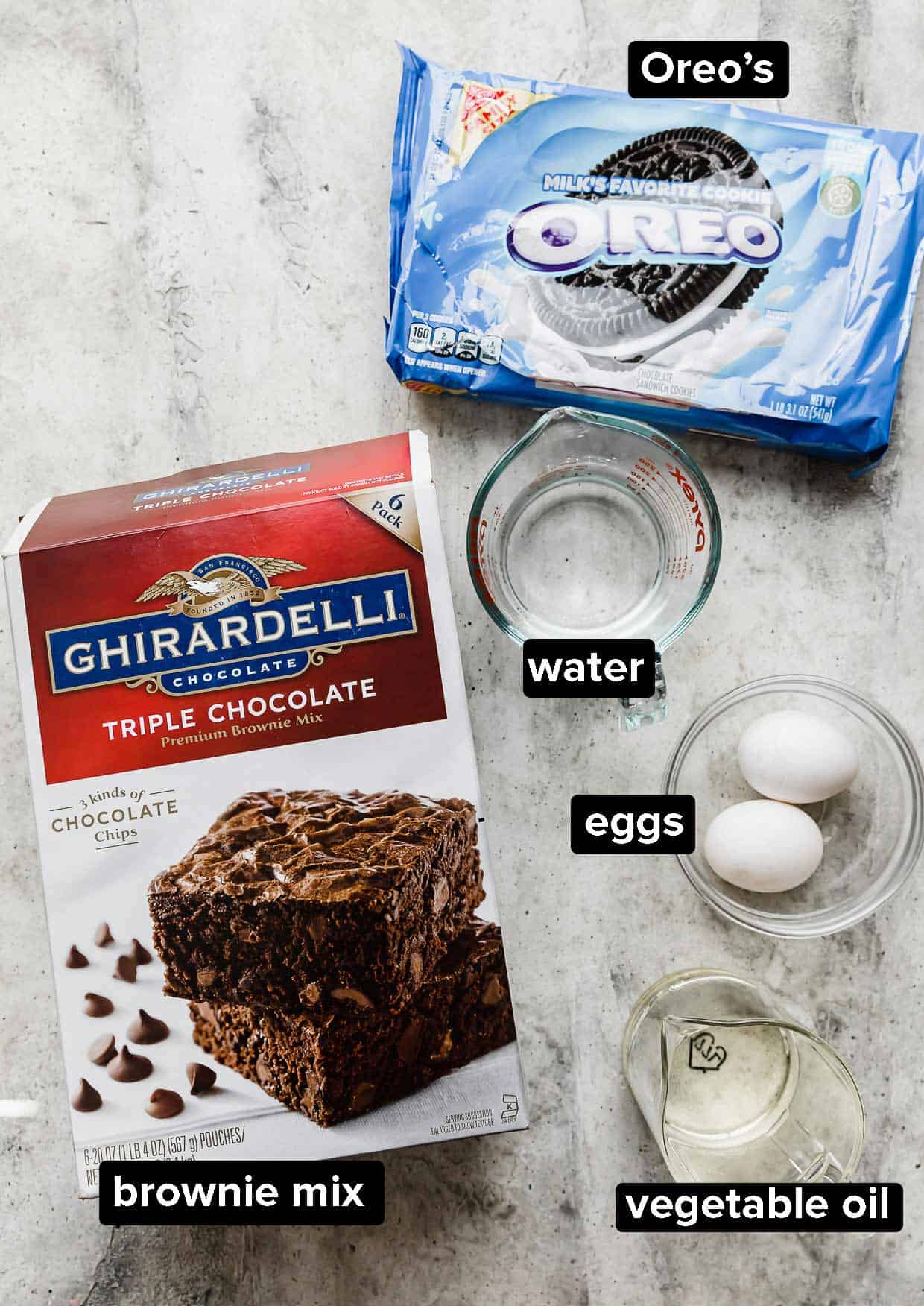 Ingredients used to make Oreo brownies on a gray background: boxed brownie mix, Oreos, water, eggs, vegetable oil.
