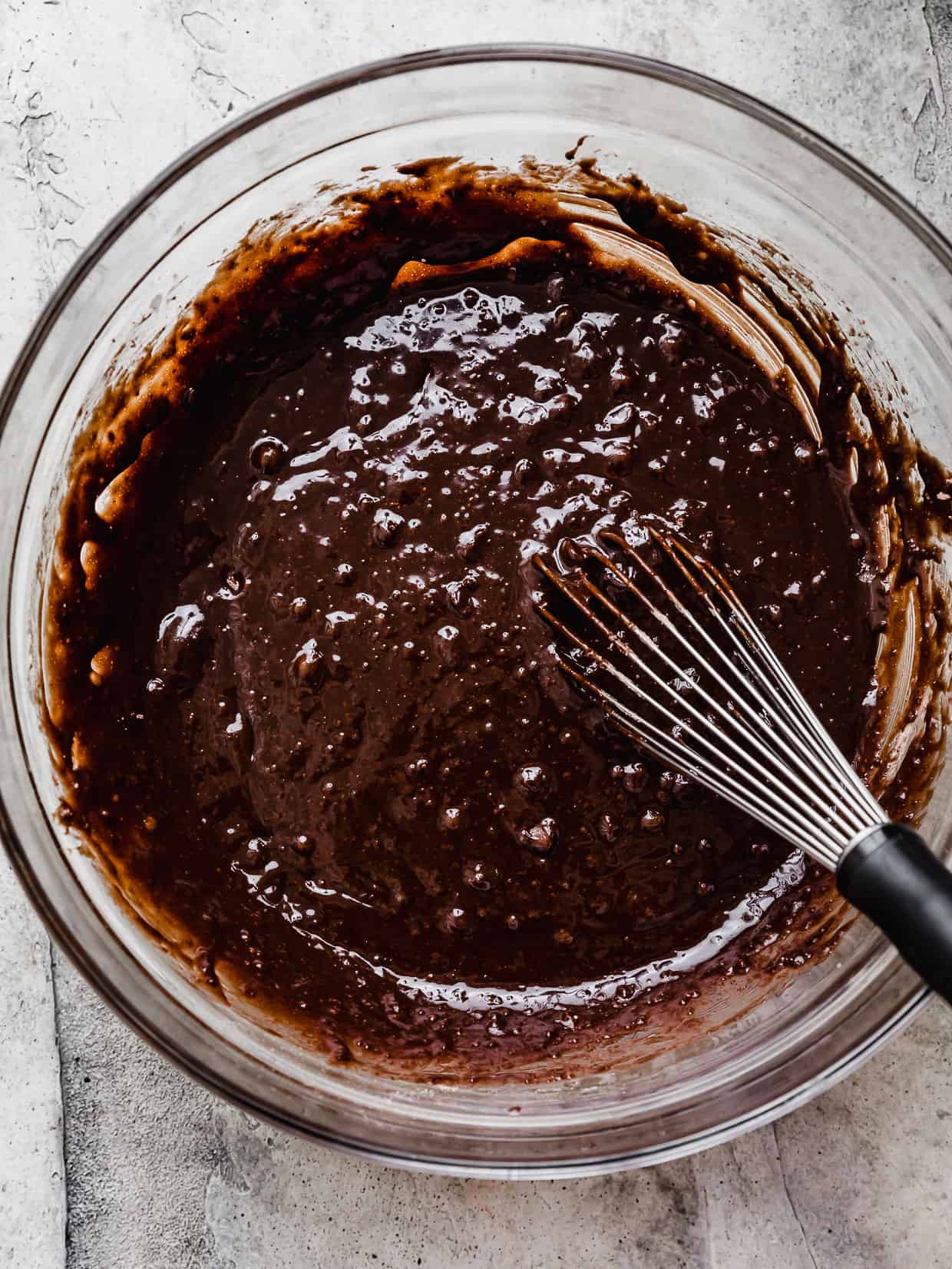A whisk mixing brownie batter in a glass bowl.