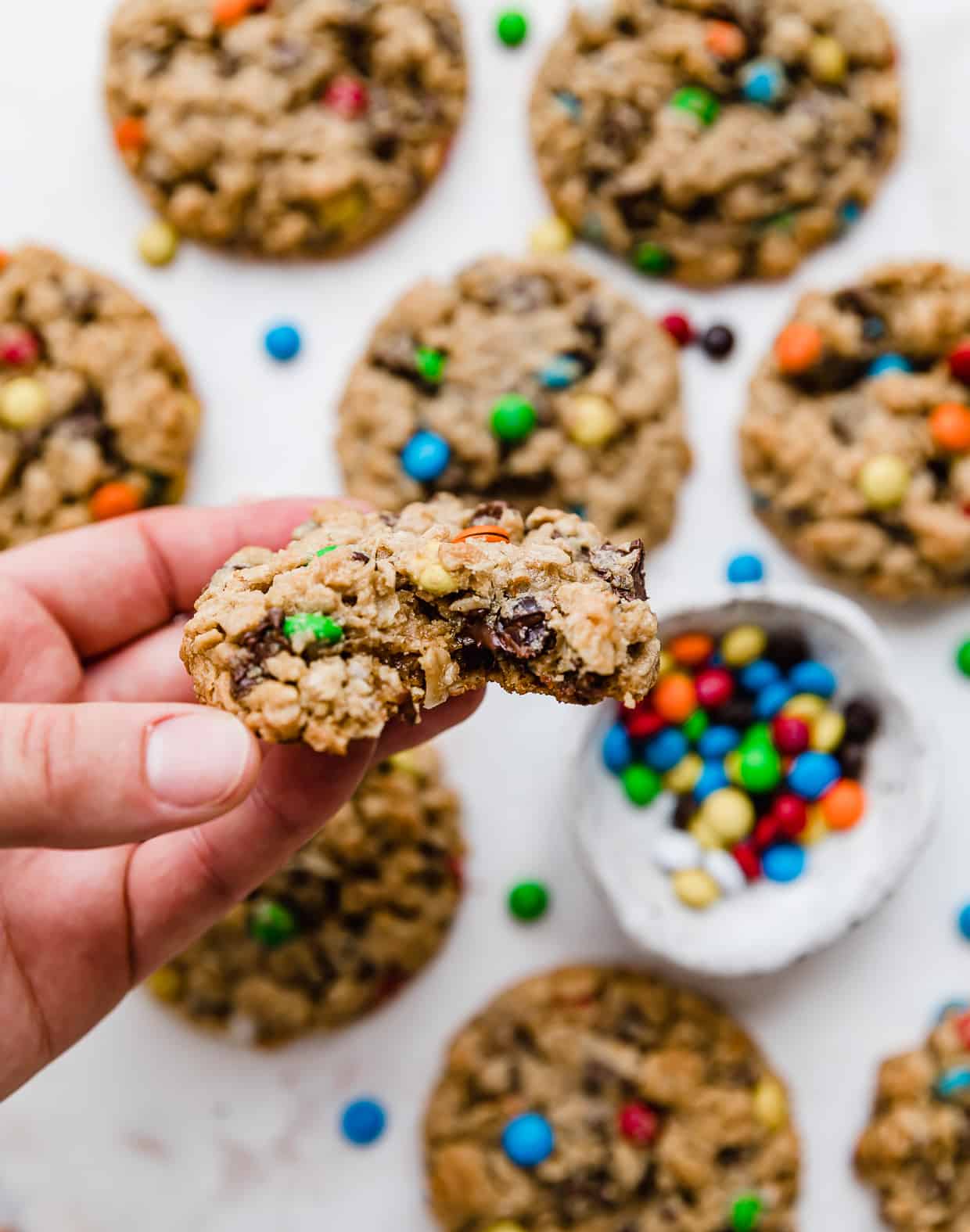 A hand holding up a monster cookie with a bite taken out of it.