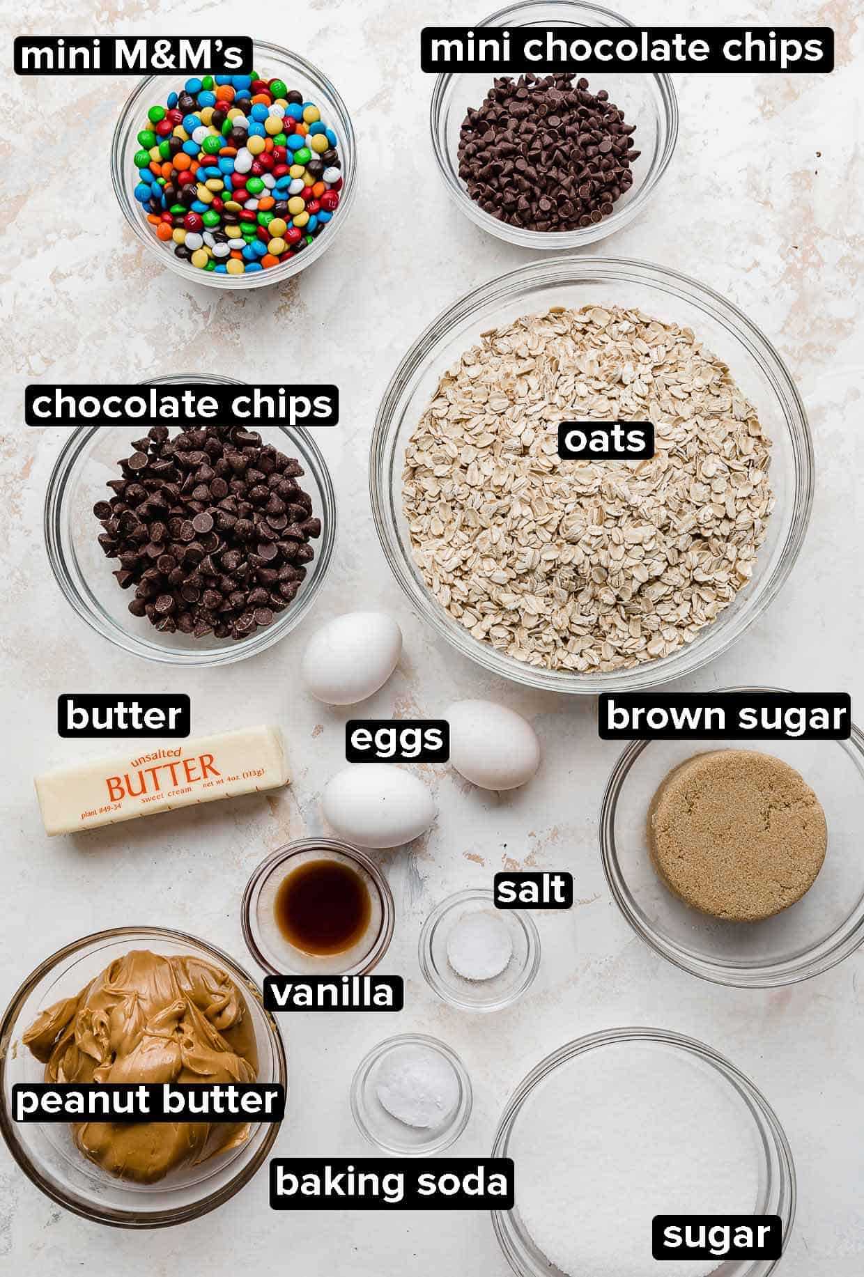 Monster cookie ingredients portioned into glass bowls on a white background.