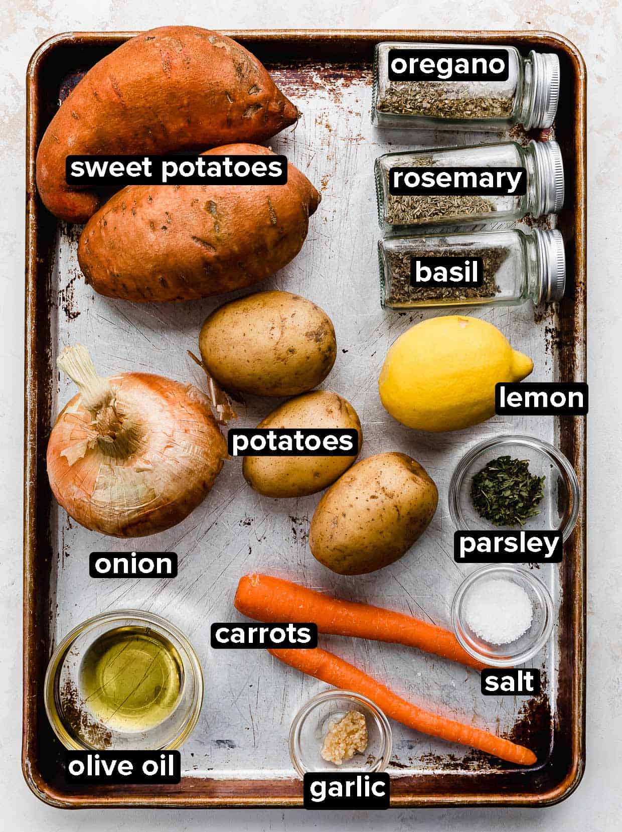 A sheet pan with ingredients used to make roasted root vegetables: sweet potato, potatoes, onion, carrots, and seasonings.