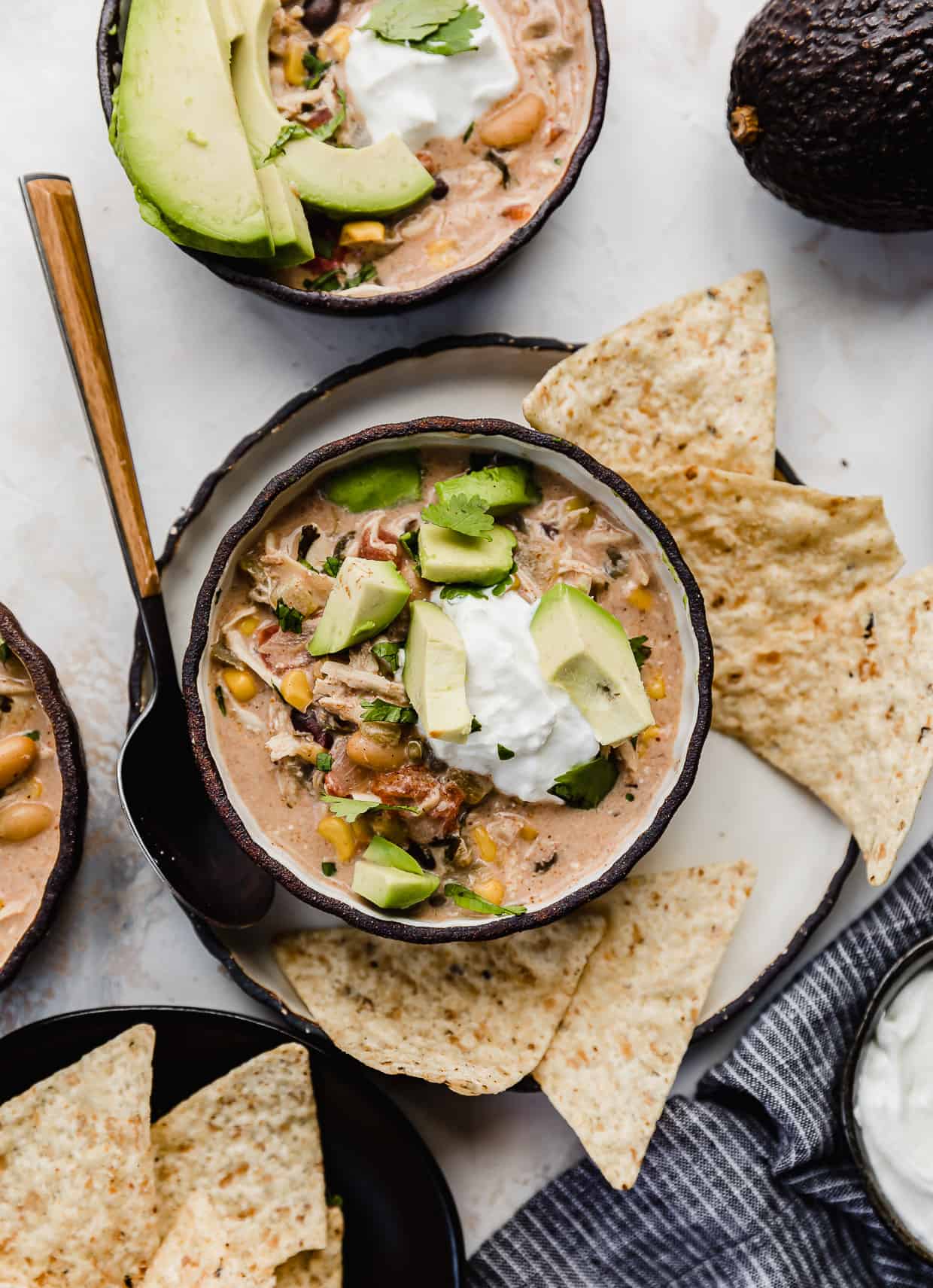 A black bowl filled with Crock Pot Cream Cheese Chicken Chili that's been topped with sour cream, avocado.
