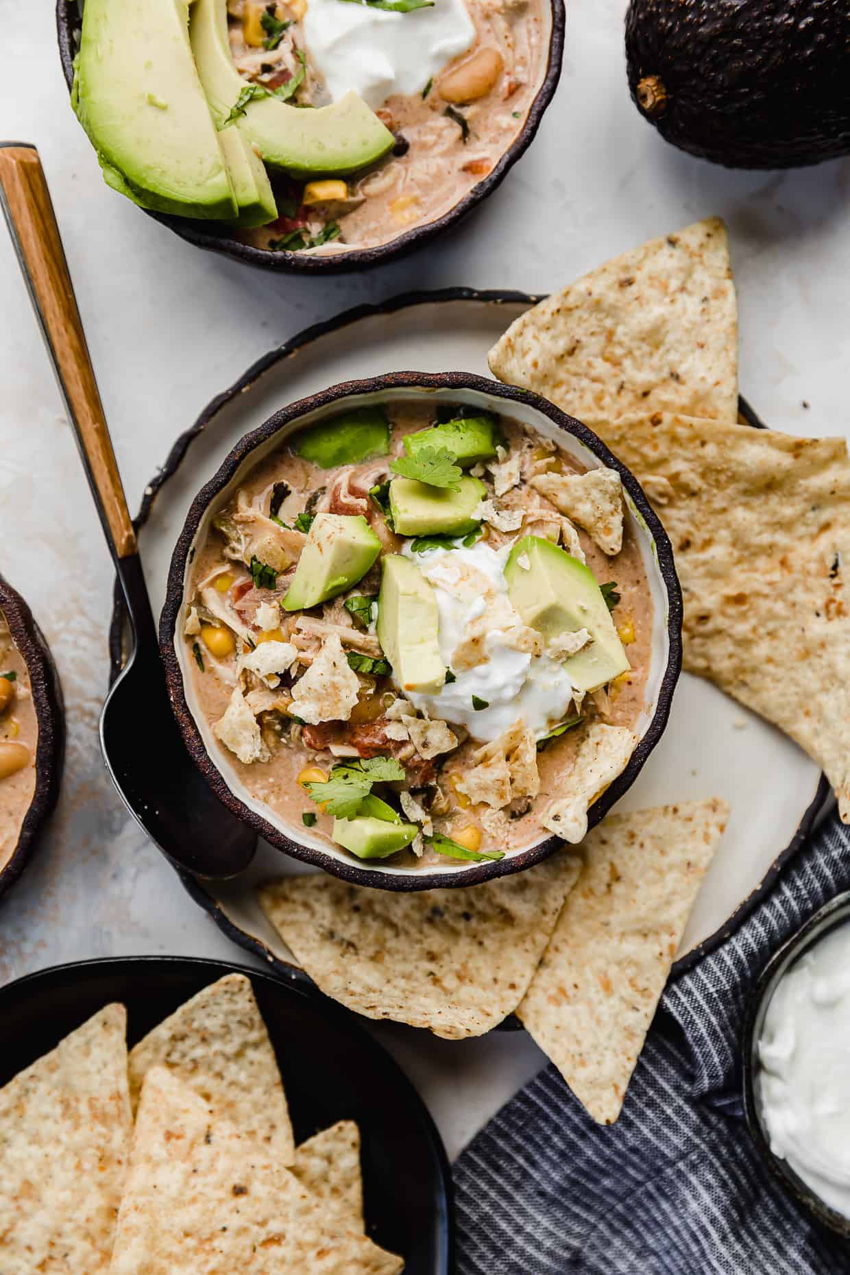 Crock Pot Cream Cheese Chicken Chili in a black bowl with tortilla chips, avocado, and sour cream on top.